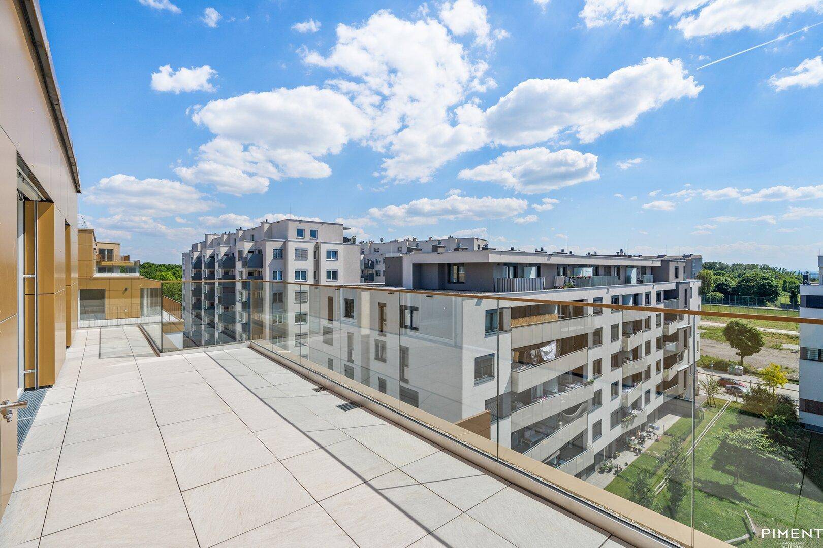 Weitläufige Dachterrasse mit Glasgeländer und Blick auf moderne Wohngebäude in der Umgebung.