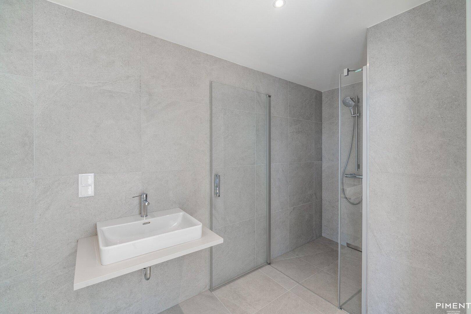 Modernes Badezimmer mit grauen Fliesen, einem Aufsatzwaschbecken und einer ebenerdigen Dusche.