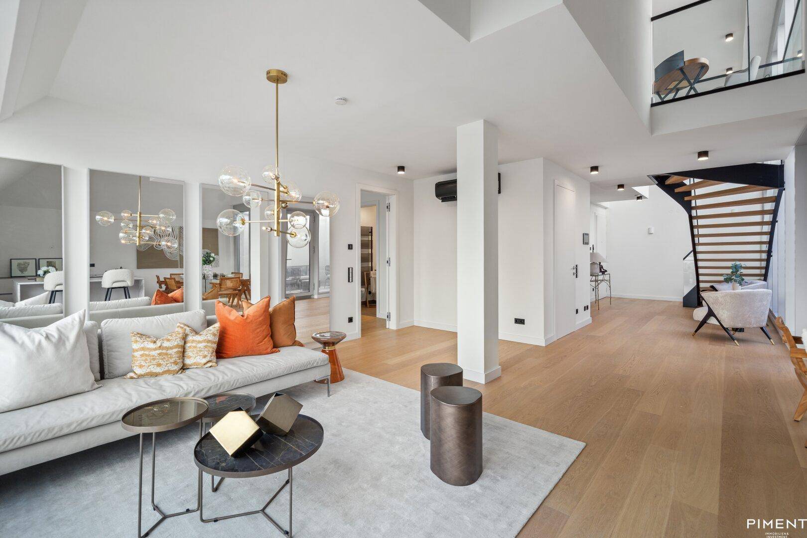 Geräumiges Wohnzimmer mit Holzboden, stilvoller Einrichtung und offener Treppe zum Obergeschoss.