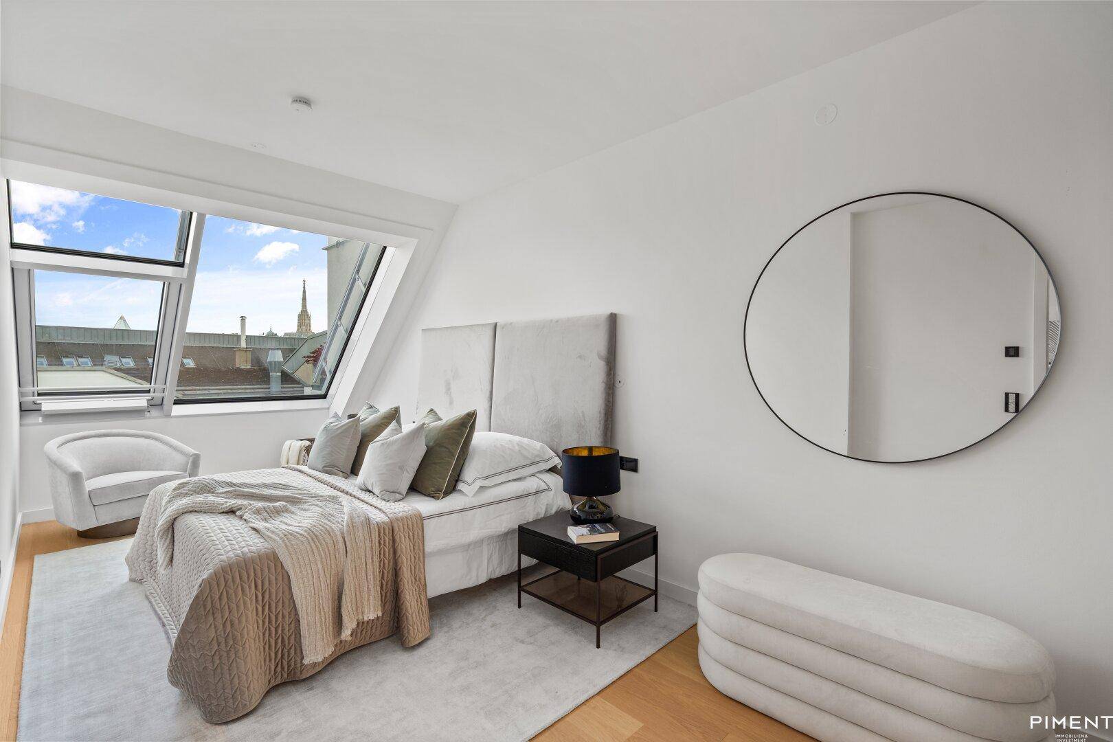 Helles Schlafzimmer mit Dachschräge, Holzboden und Blick auf die Stadt durch das Fenster.