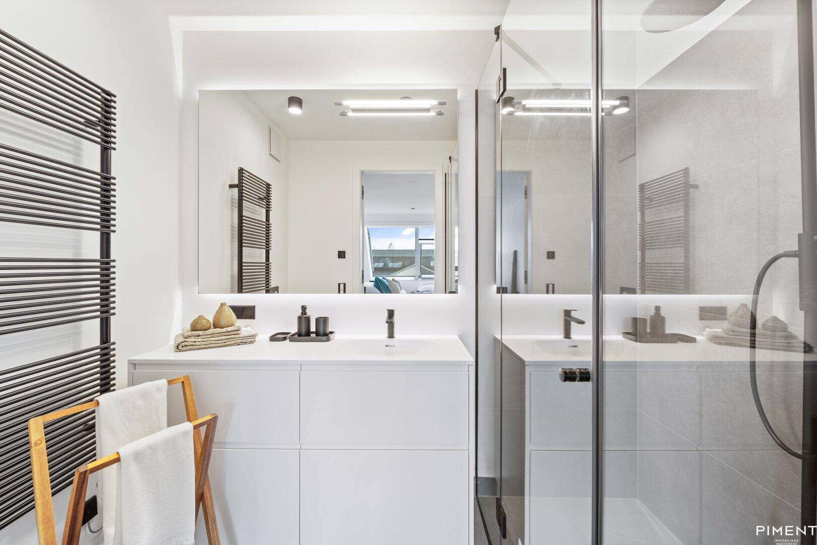 Modernes Badezimmer mit Einzelwaschbecken, beleuchtetem Spiegel und begehbarer Dusche.