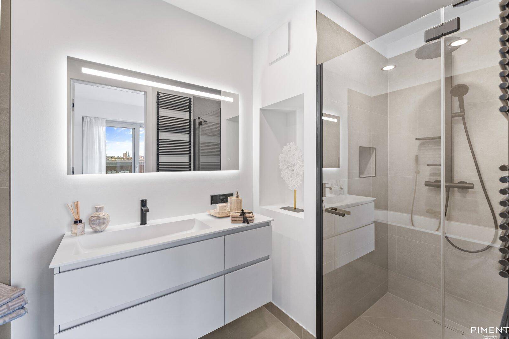 Elegantes Badezimmer mit Waschtisch, beleuchtetem Spiegel und kombinierter Dusch-Badewanne.