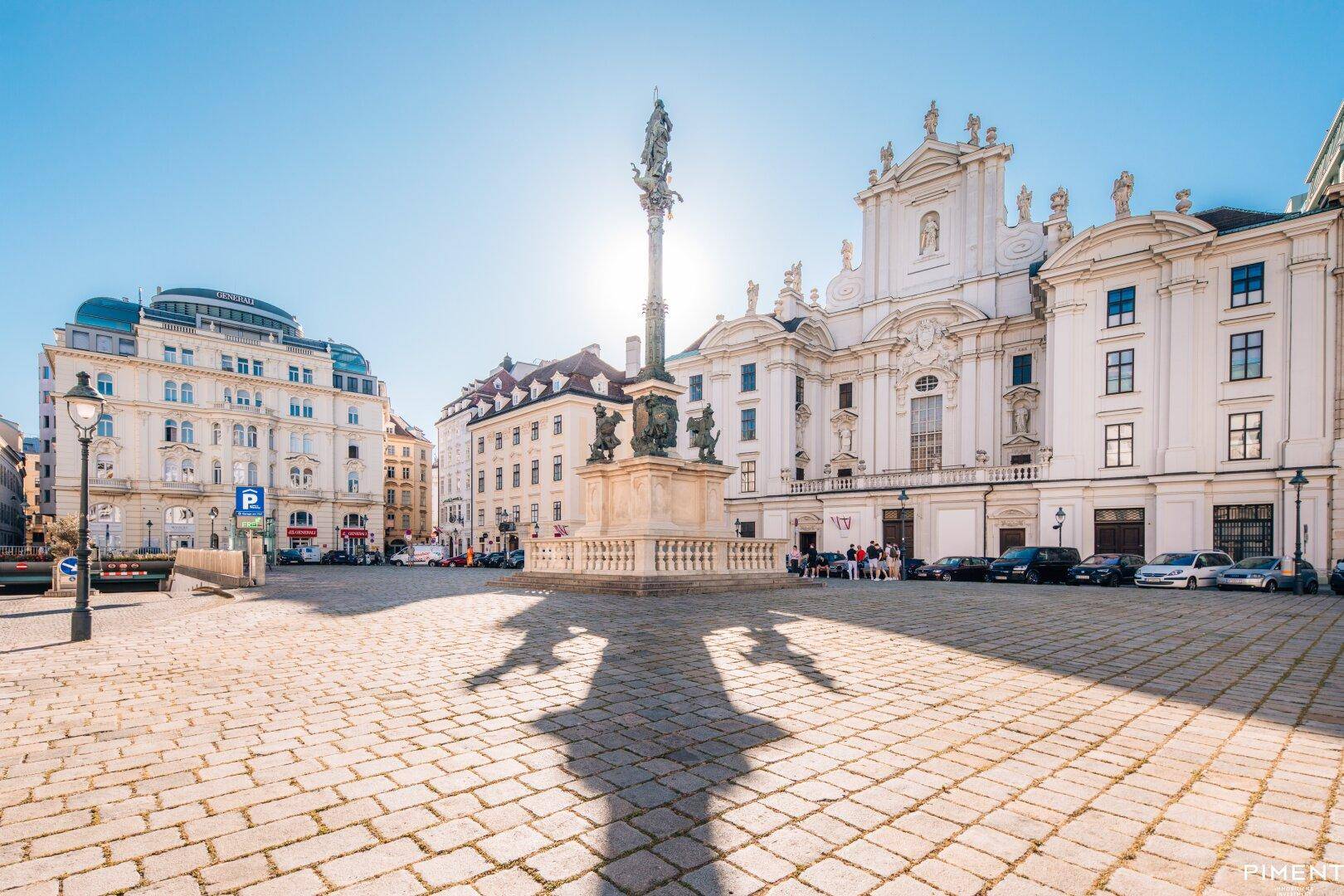 Historischer Stadtplatz mit einer imposanten Säule und prächtigen Gebäuden unter blauem Himmel.
