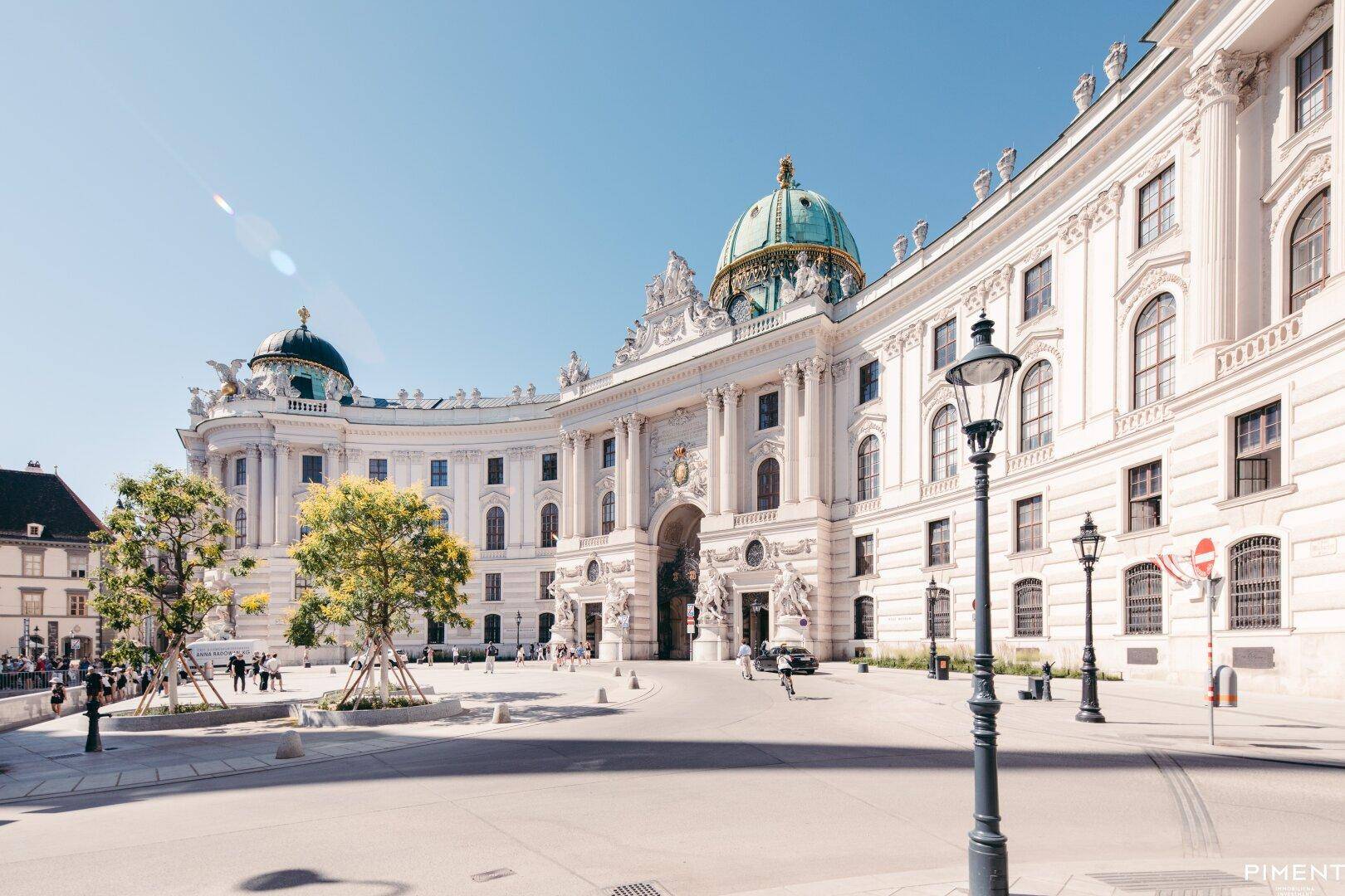 Beeindruckendes historisches Gebäude mit Kuppeln und Säulen an einem sonnigen Stadtplatz.