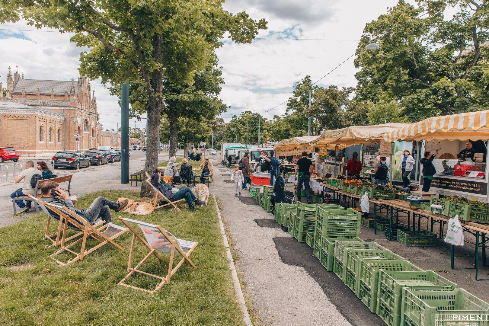 Lebhafter Wochenmarkt im Freien mit Verkaufsständen und Menschen, die sich auf Liegestühlen entspannen.