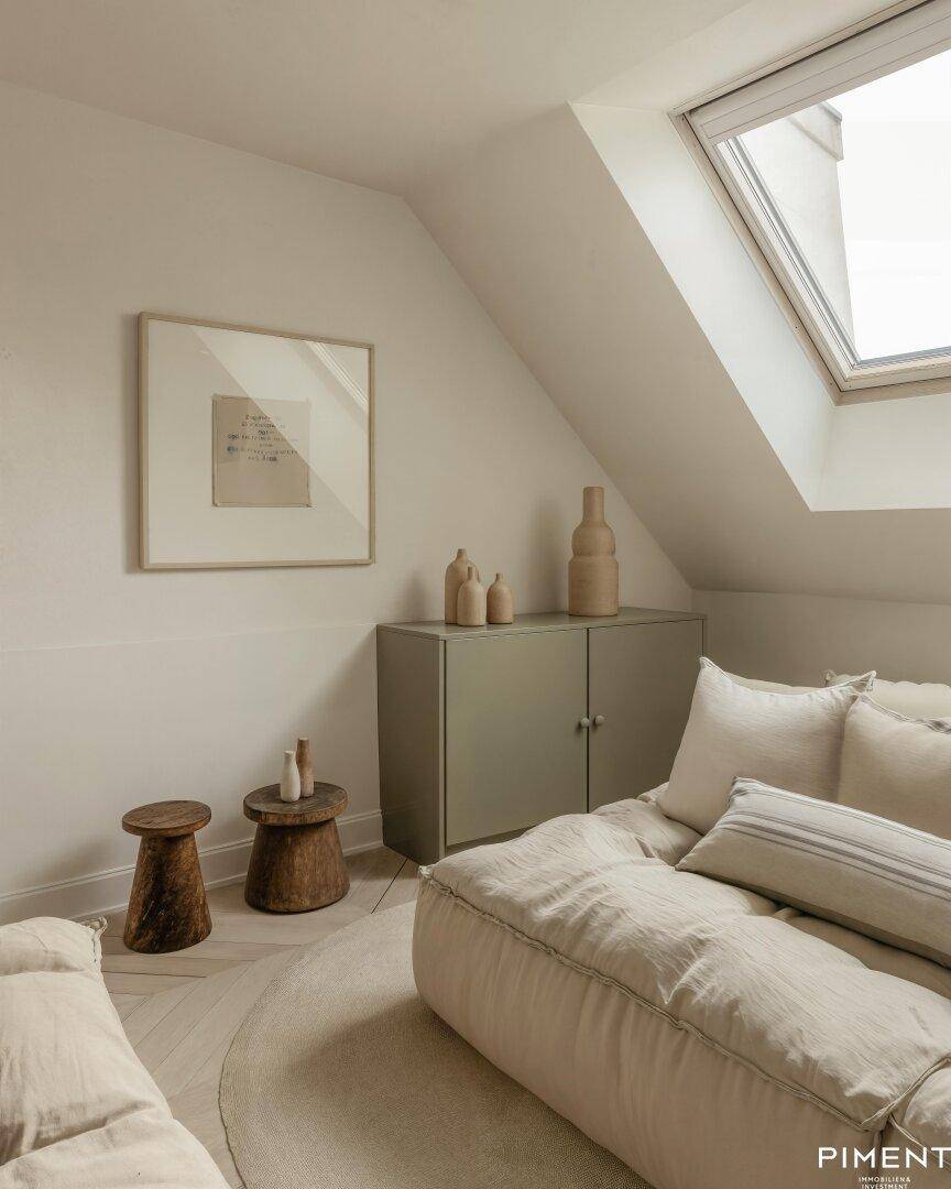 Gemütlicher Dachbodenraum mit schräger Decke, Dachfenster und weichen Sitzgelegenheiten.