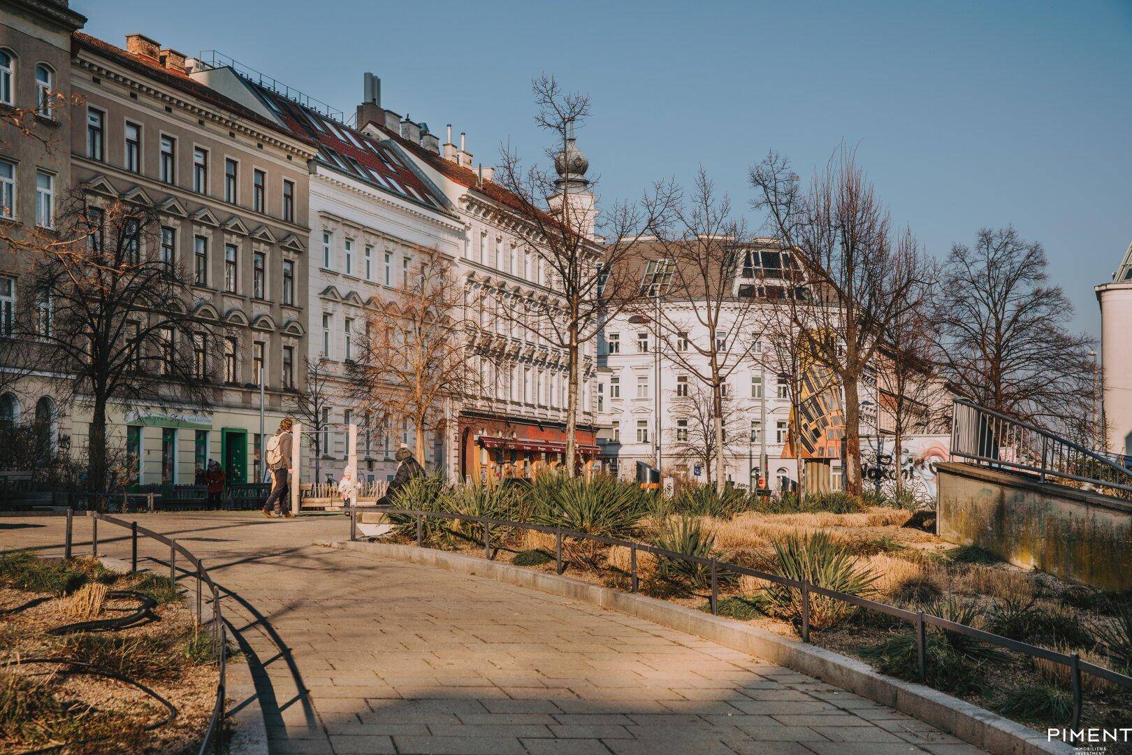 Historische Gebäude entlang einer Straße mit einem begrünten Parkbereich im Vordergrund.