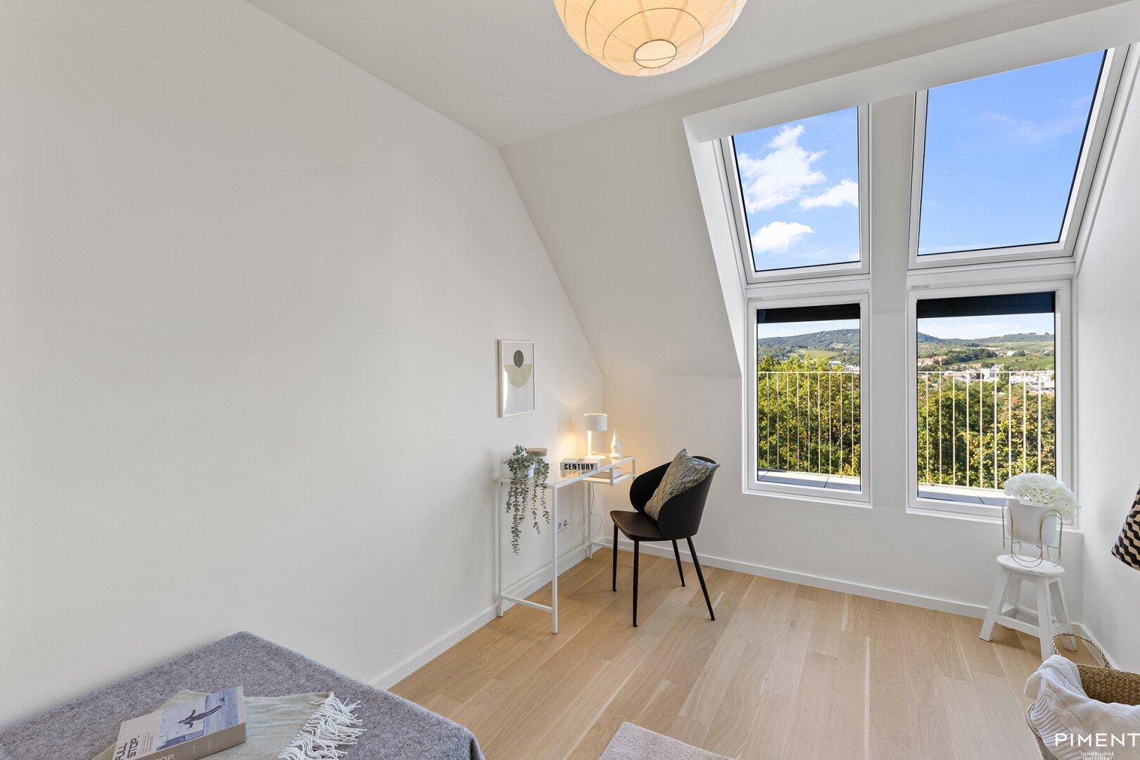 Helles Zimmer mit Holzboden, Dachfenstern und einem Arbeitsbereich mit Blick ins Grüne.