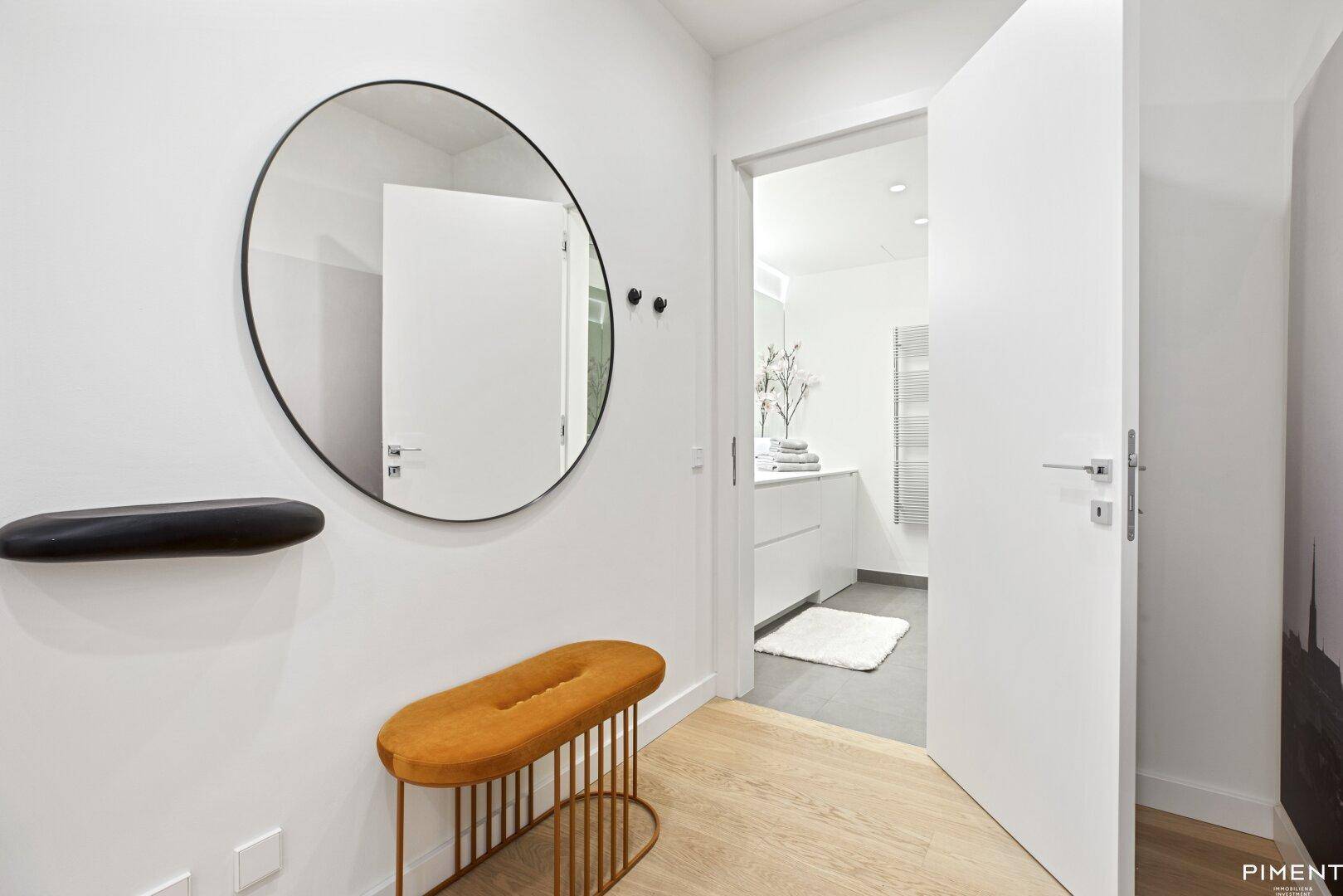 Heller Flur mit modernem Spiegel, Sitzbank und offenem Zugang zu einem Badezimmer.