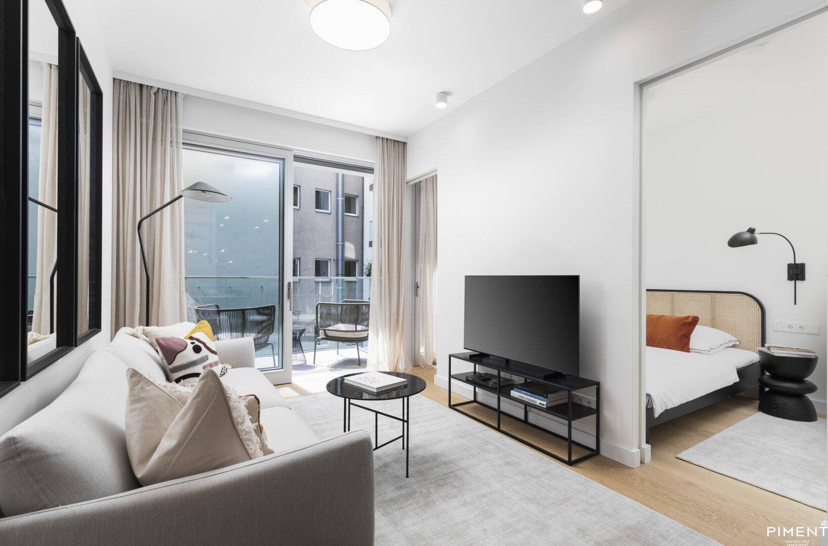 Gemütliches Wohnzimmer mit Sofa, Fernseher und direktem Zugang zu einem möblierten Balkon.