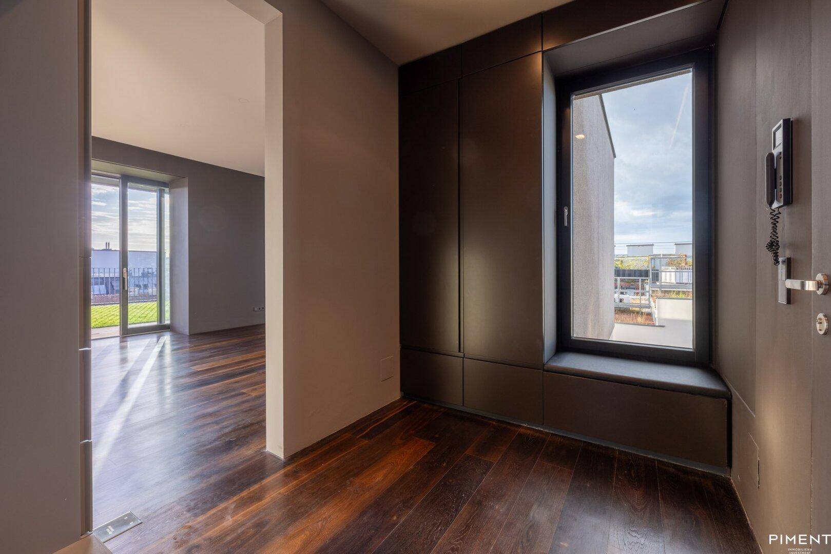 Eingangsbereich mit dunklem Holzfußboden, Fensterbank und Gegensprechanlage, bietet einen ersten Blick auf die Wohnung.