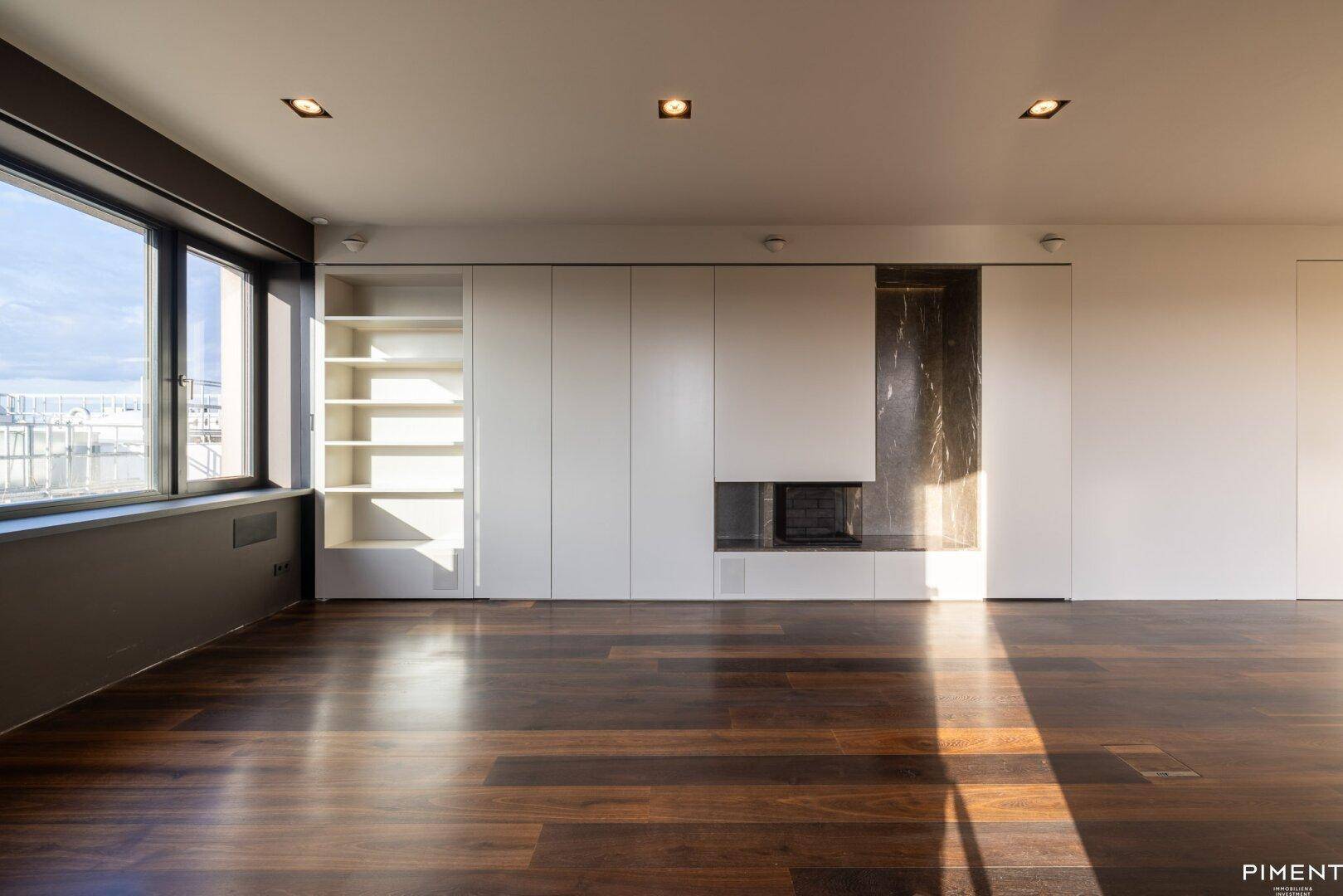 Helles Wohnzimmer mit dunklem Holzfußboden, Einbauschränken, Kamin und weitem Blick über die Stadt.
