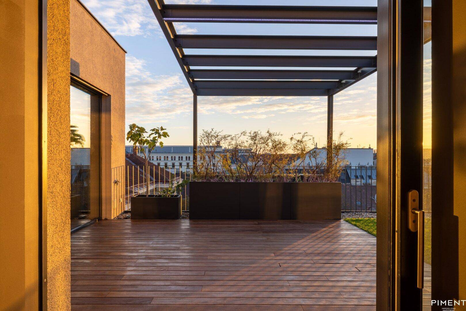 Blick von innen auf die Dachterrasse mit Pergola und Pflanzen bei wunderschönem Sonnenuntergang.