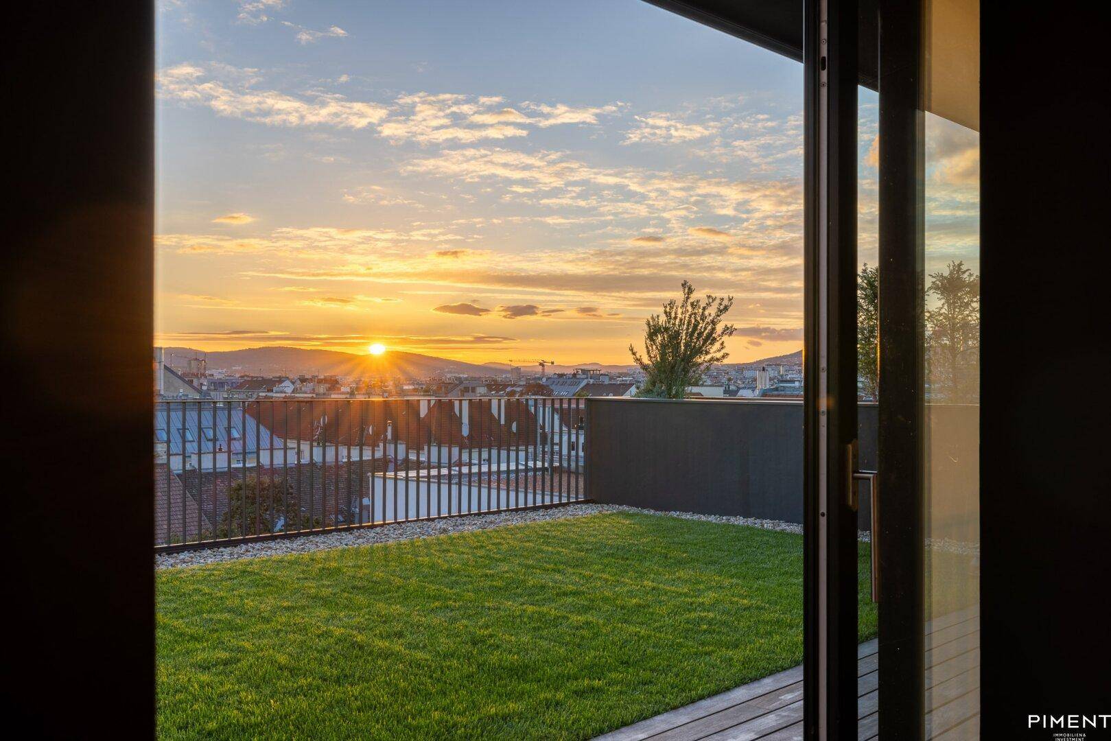 Atemberaubender Blick von innen auf die grüne Dachterrasse und die Stadtlandschaft im warmen Abendlicht.