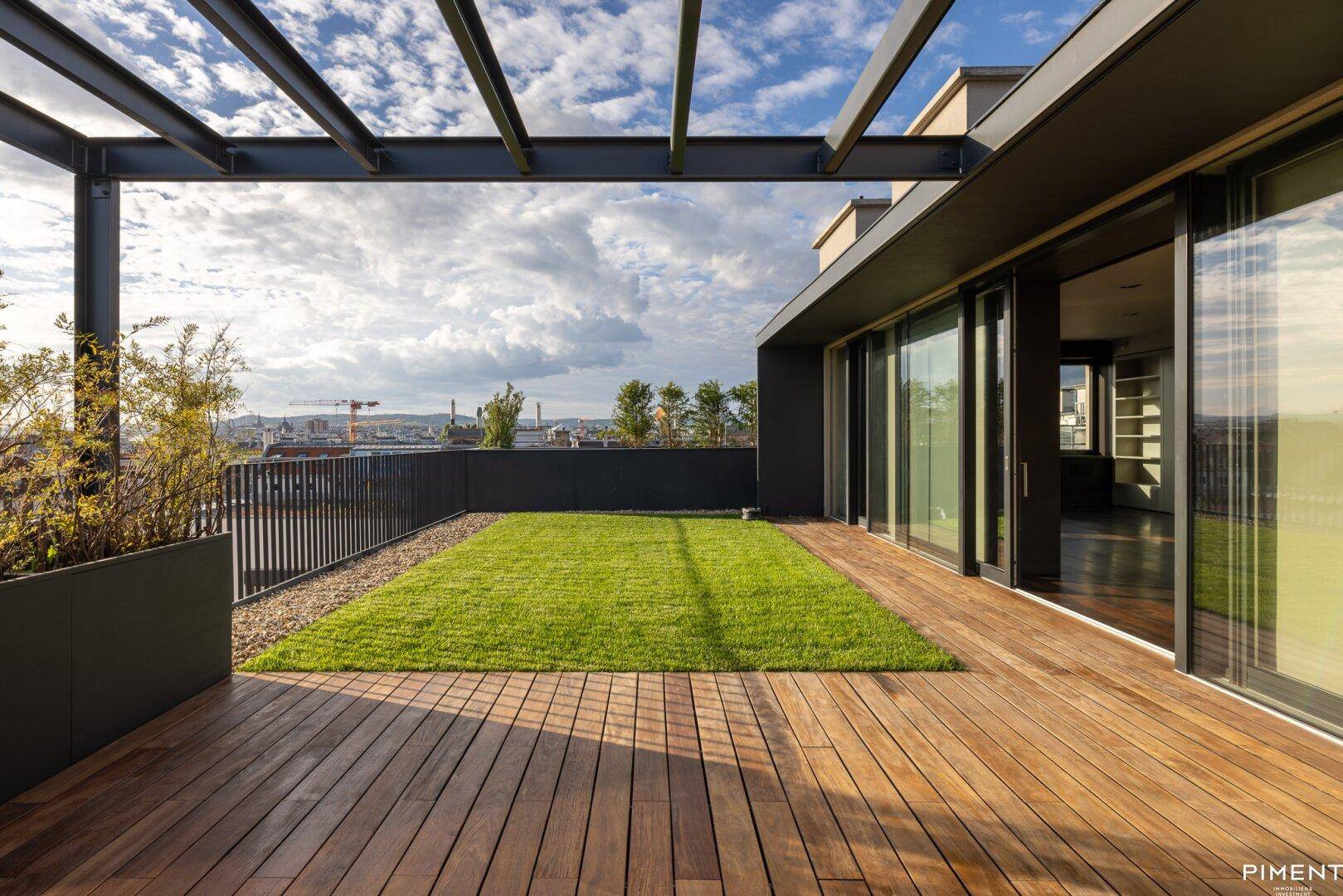 Geräumige Dachterrasse mit Holzbelag, Rasenfläche und Blick über die Stadt unter bewölktem Himmel.