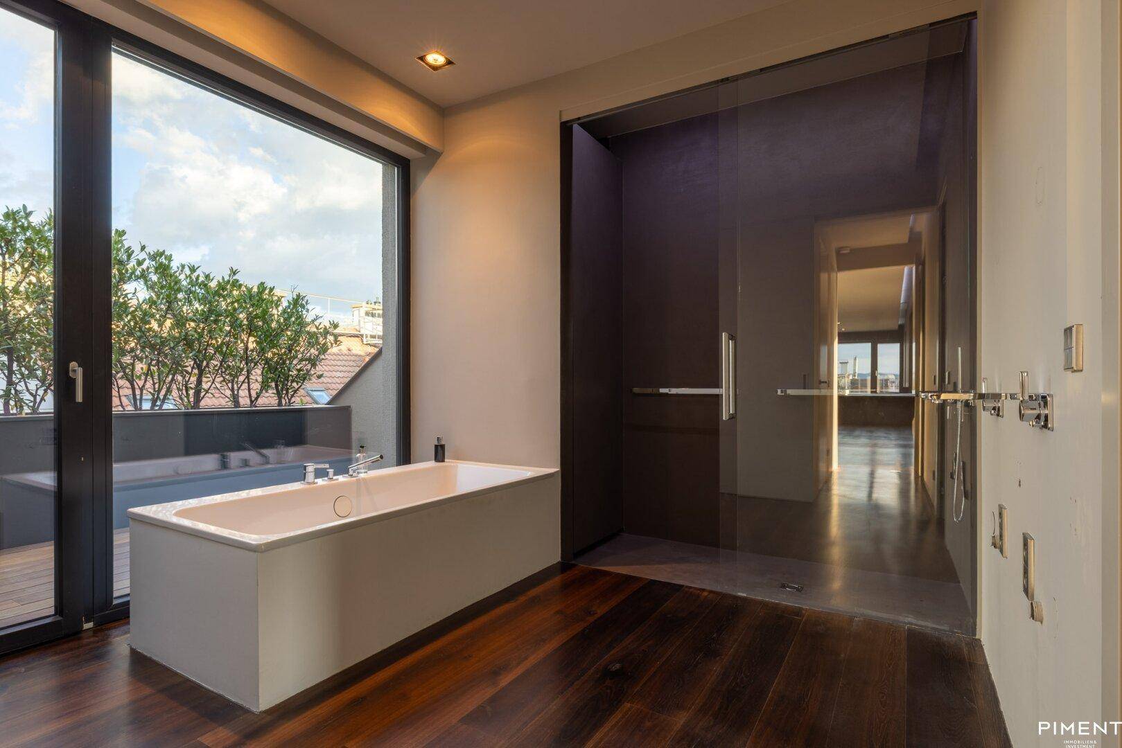 Luxuriöses Badezimmer mit Badewanne, großer Fensterfront und begehbarer Dusche, bietet viel Tageslicht.