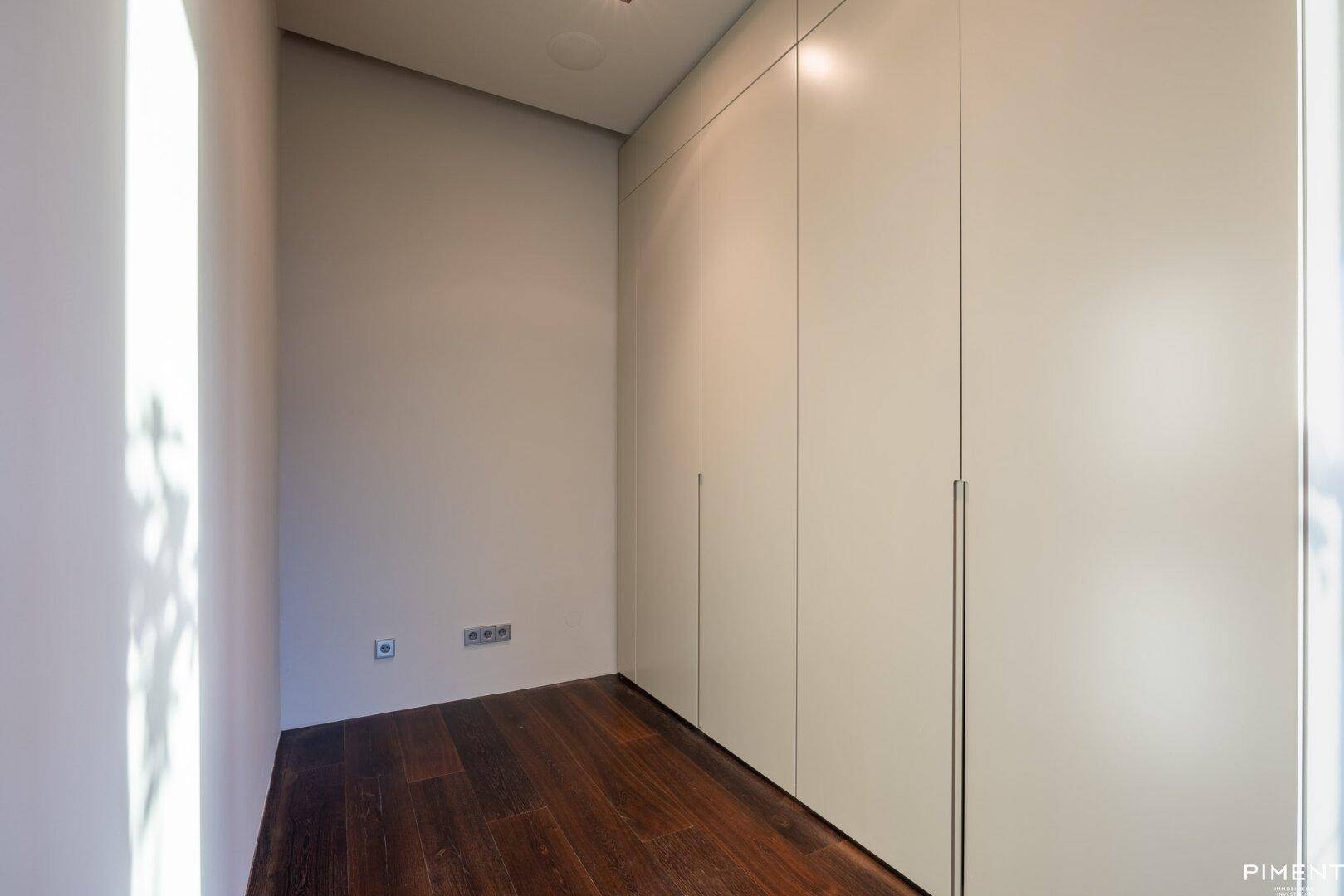 Kleiner Raum mit dunklem Holzfußboden und praktischen weißen Einbauschränken für Stauraum.
