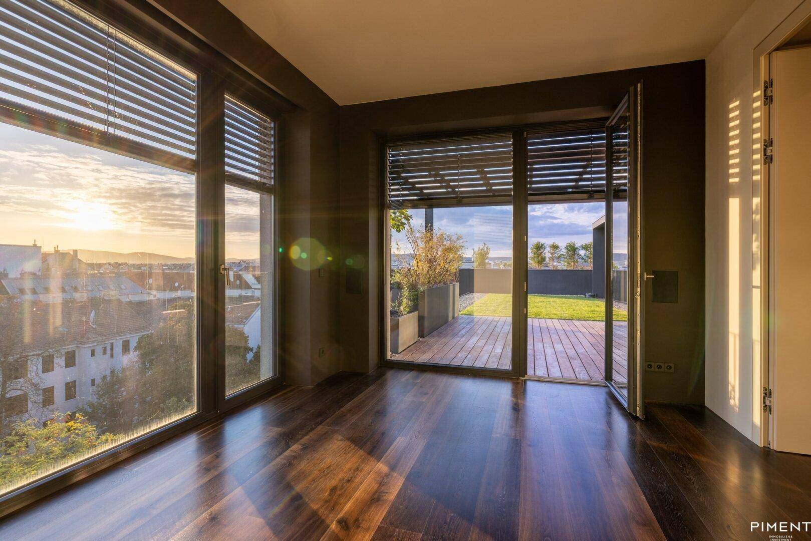 Heller Innenraum mit dunklem Parkettboden, großen Fenstern und Zugang zur Dachterrasse.
