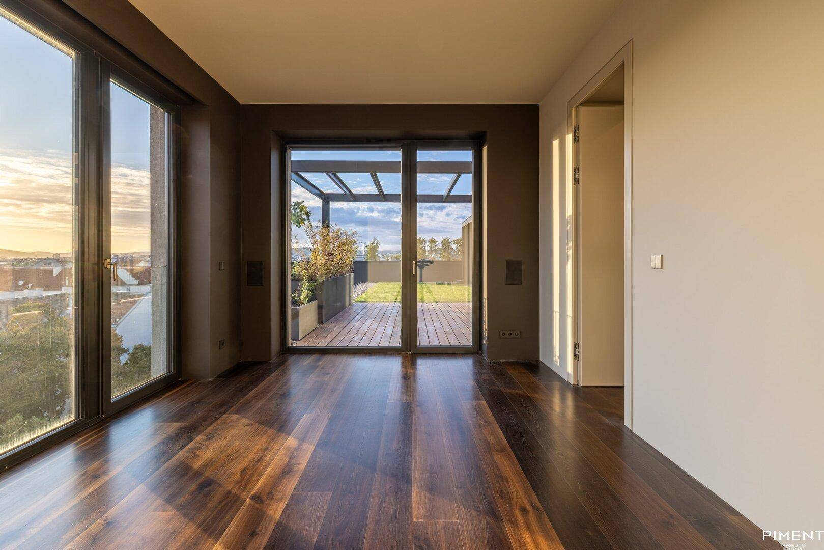 Heller Raum mit dunklem Holzfußboden, großen Fenstern und direktem Zugang zur Dachterrasse.