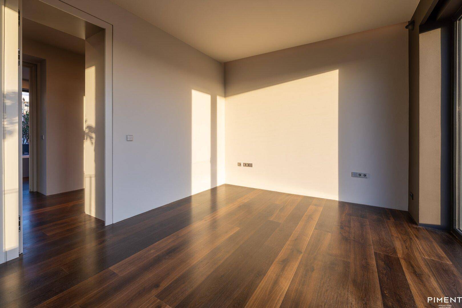 Heller Raum mit dunklem Holzfußboden und viel natürlichem Licht, ideal als Schlaf- oder Arbeitszimmer.