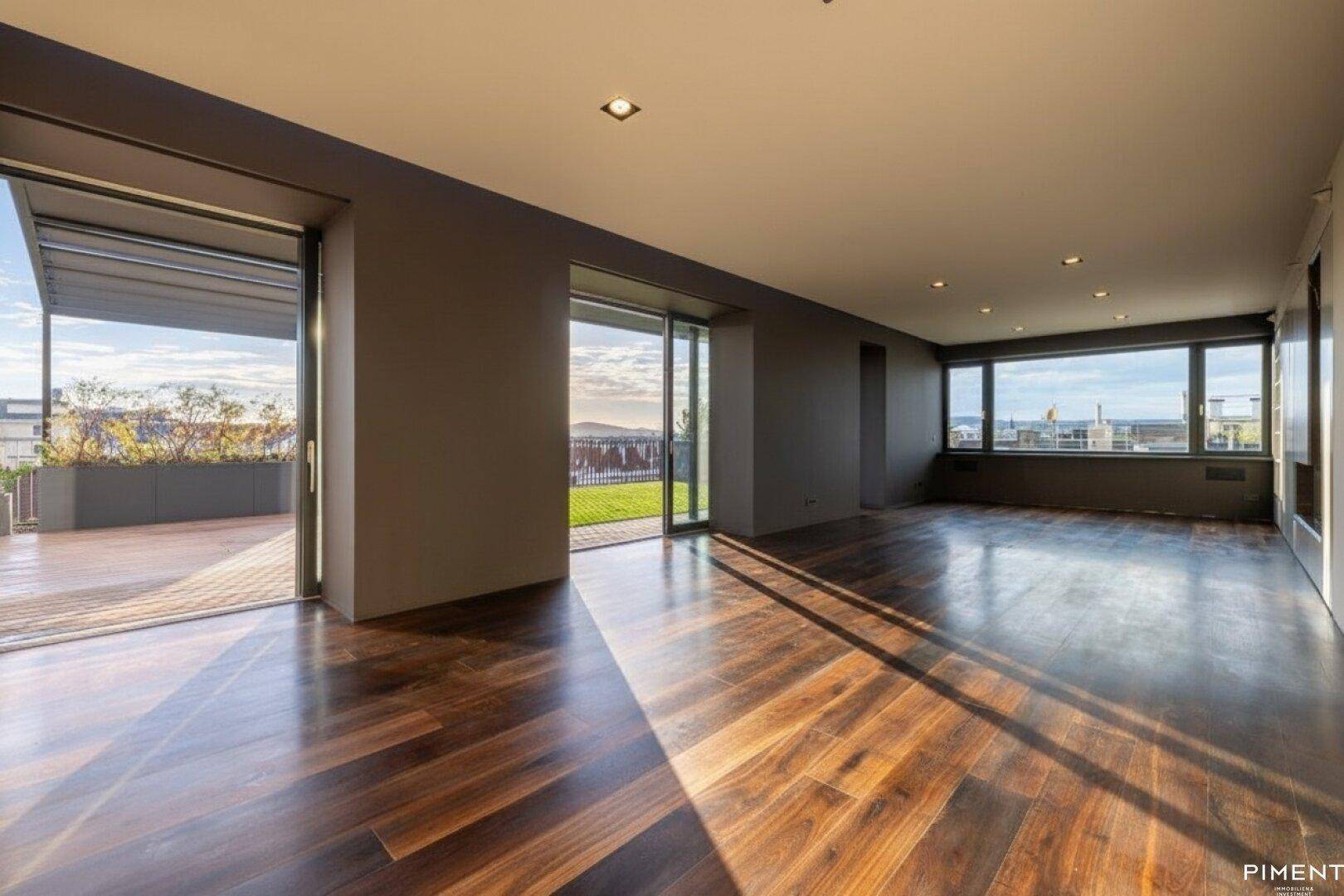 Geräumiges Wohnzimmer mit dunklem Holzfußboden, großen Fenstern und sonnigem Zugang zur Dachterrasse.