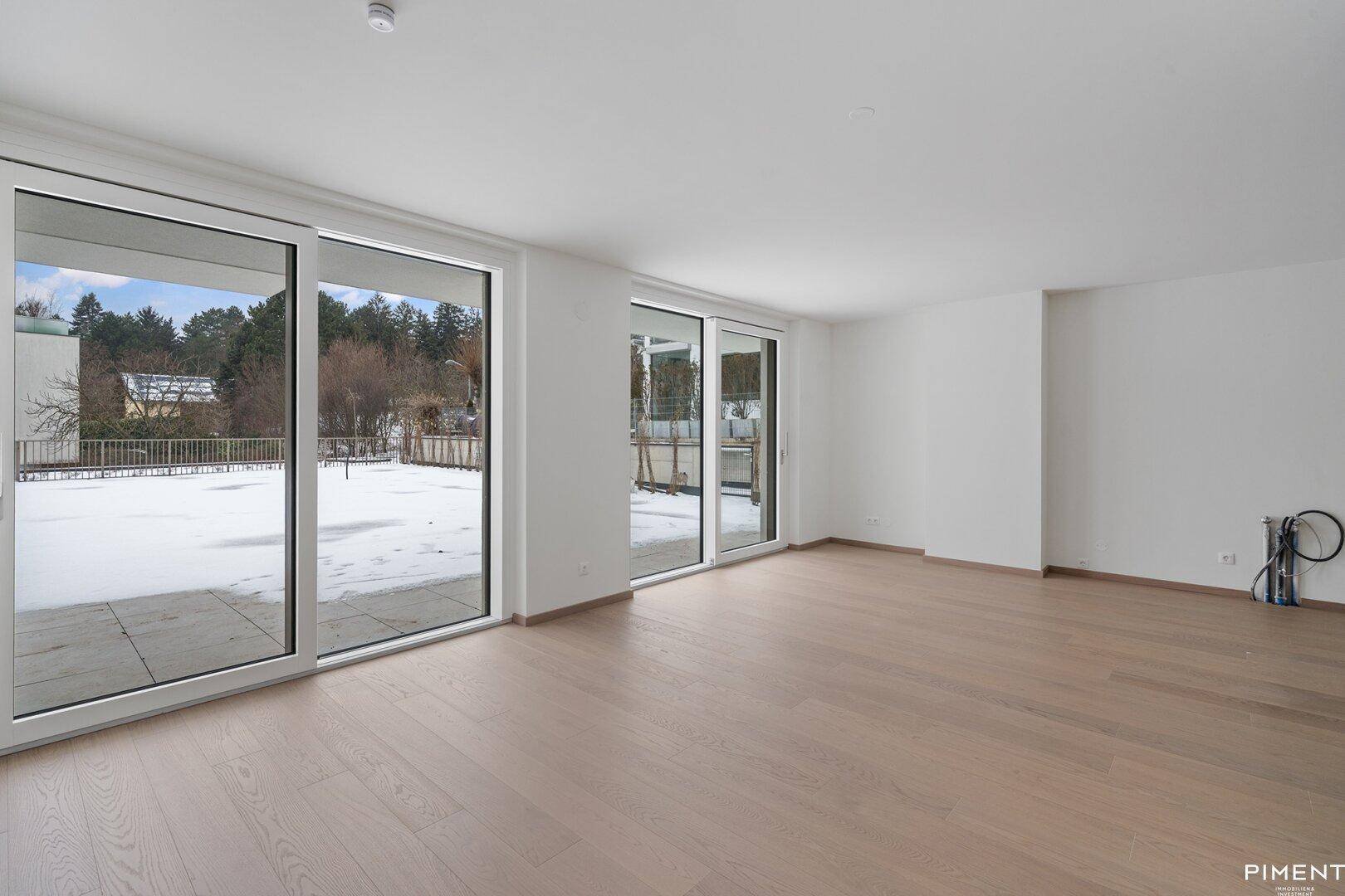 Helles, leeres Wohnzimmer mit großen Schiebetüren, die zu einer verschneiten Terrasse und Garten führen.