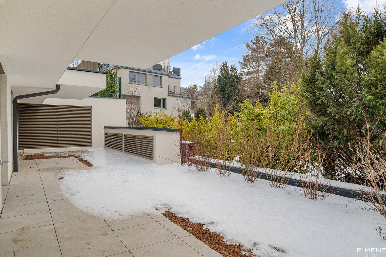 Gepflasterte Terrasse mit Schnee und umgebender Bepflanzung, die einen ruhigen Außenbereich bildet.