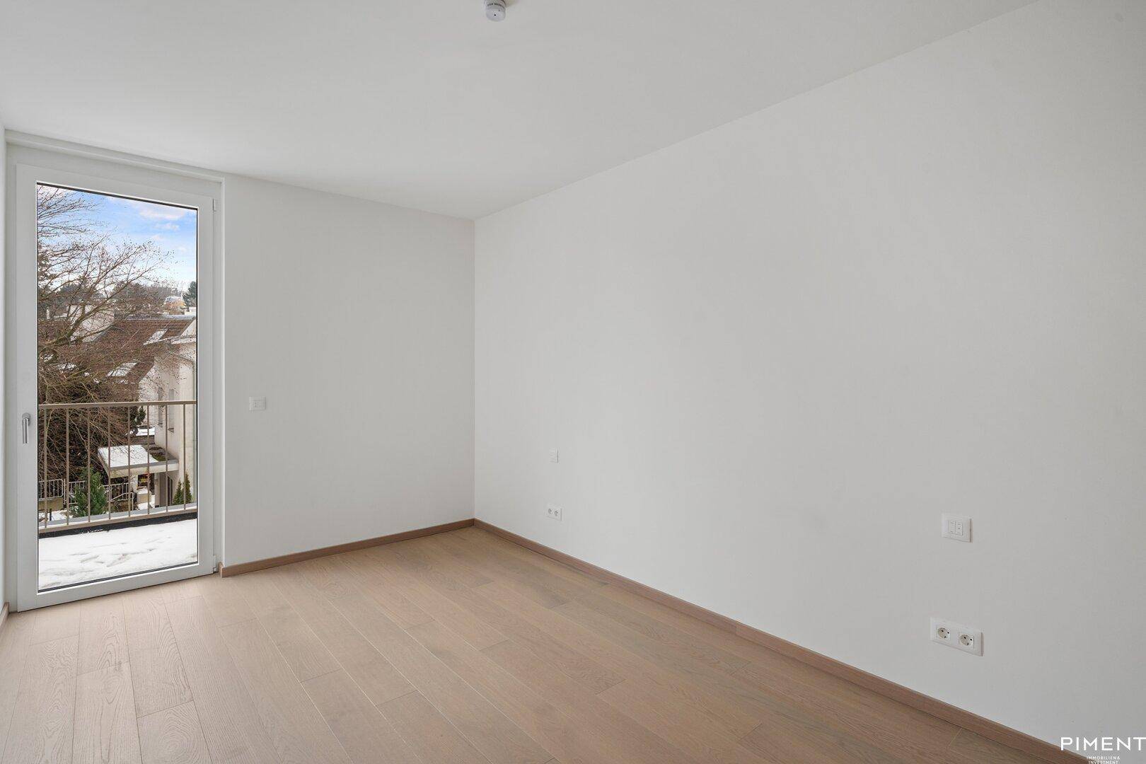 Helles Schlafzimmer mit Holzboden und französischem Balkon, ideal für natürliche Belüftung.