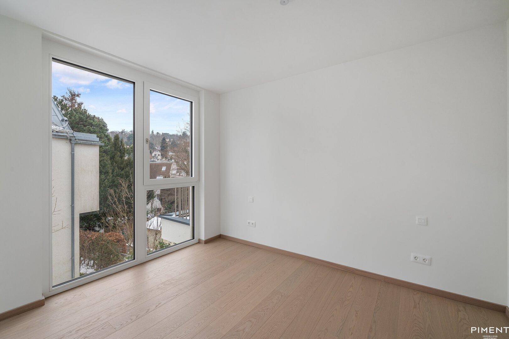 Geräumiges Schlafzimmer mit großen Fenstern und hellem Parkettboden, bietet viel Tageslicht.