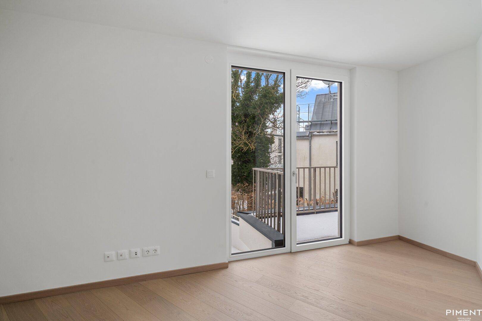 Helles Zimmer mit Zugang zu einem kleinen Balkon und Blick auf die umliegende Bebauung.