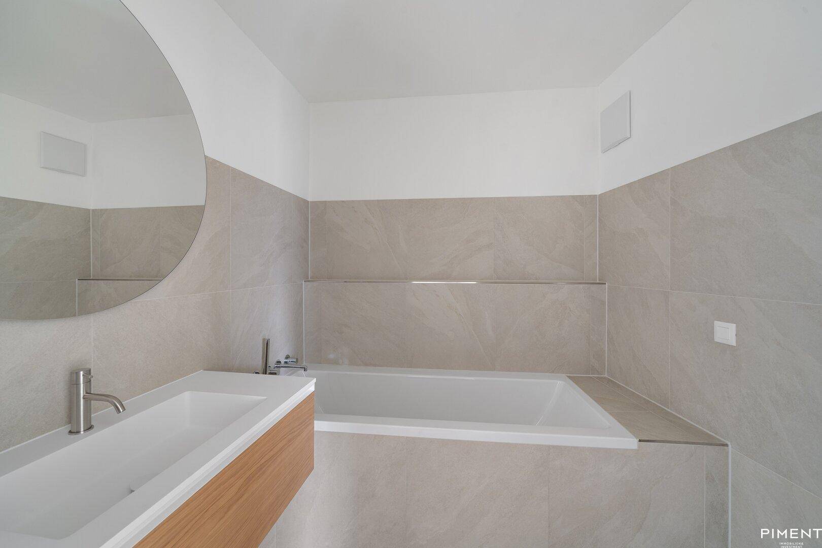 Modernes Badezimmer mit Badewanne, Einzelwaschbecken und großen grauen Fliesen.