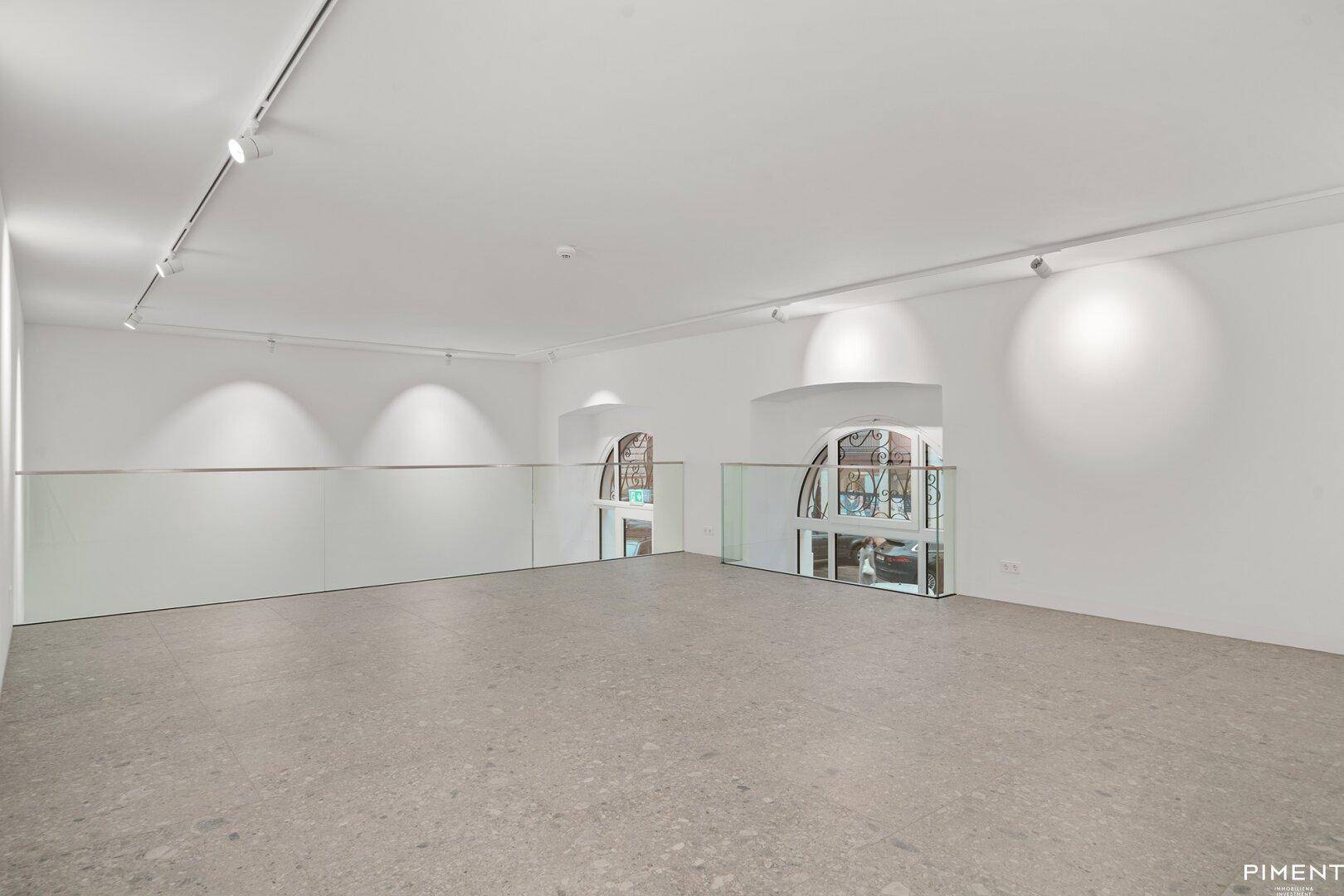 Offener Gewerberaum mit großen Bogenfenstern, hohen Decken und moderner Glasbrüstung.