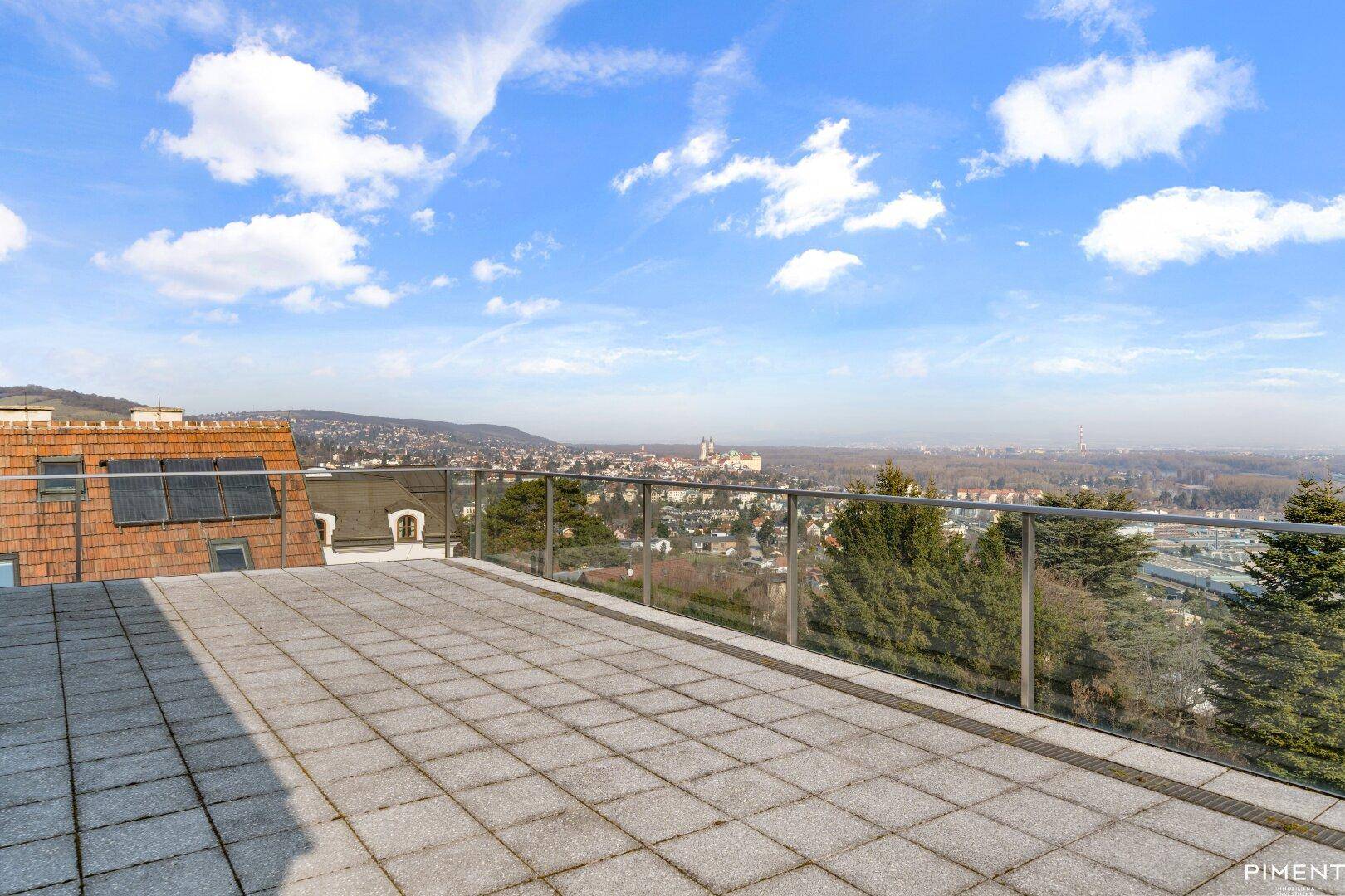 Weitläufige Dachterrasse mit Steinplatten und Glasgeländer, bietet einen spektakulären Panoramablick über die Stadt.