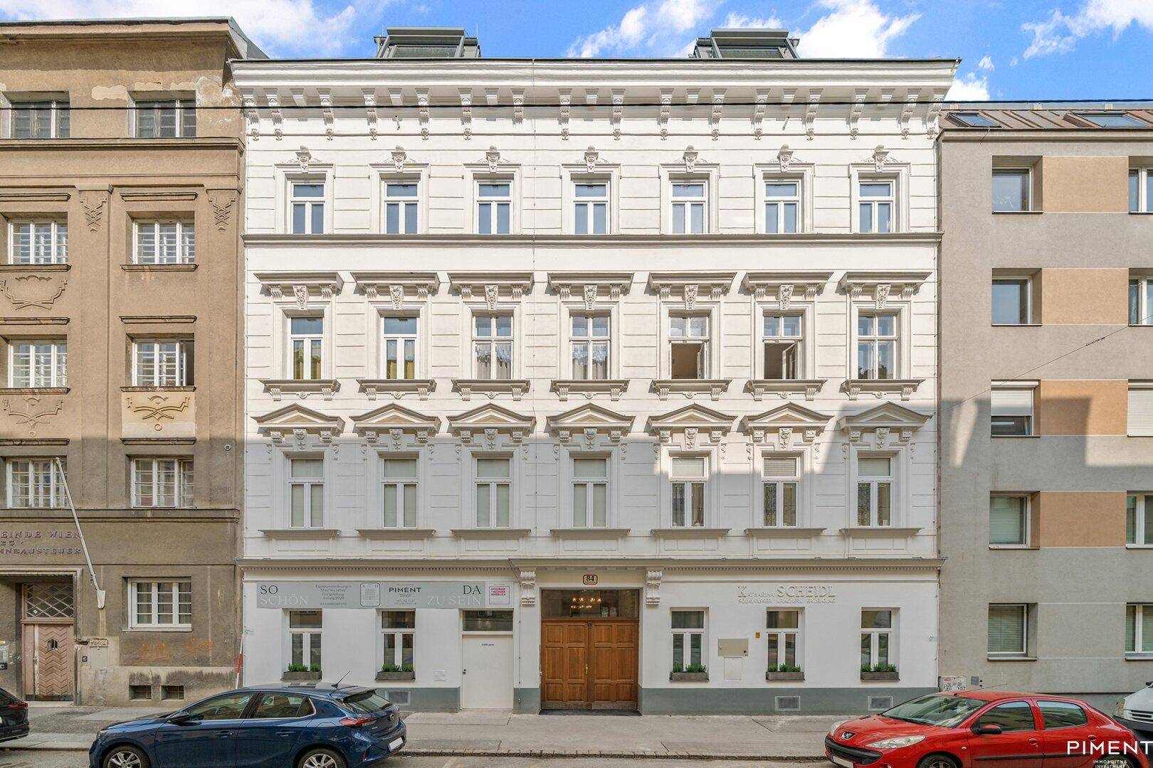 Historische Altbaufassade mit reich verzierten Fenstern und weißem Anstrich an einer Straße.