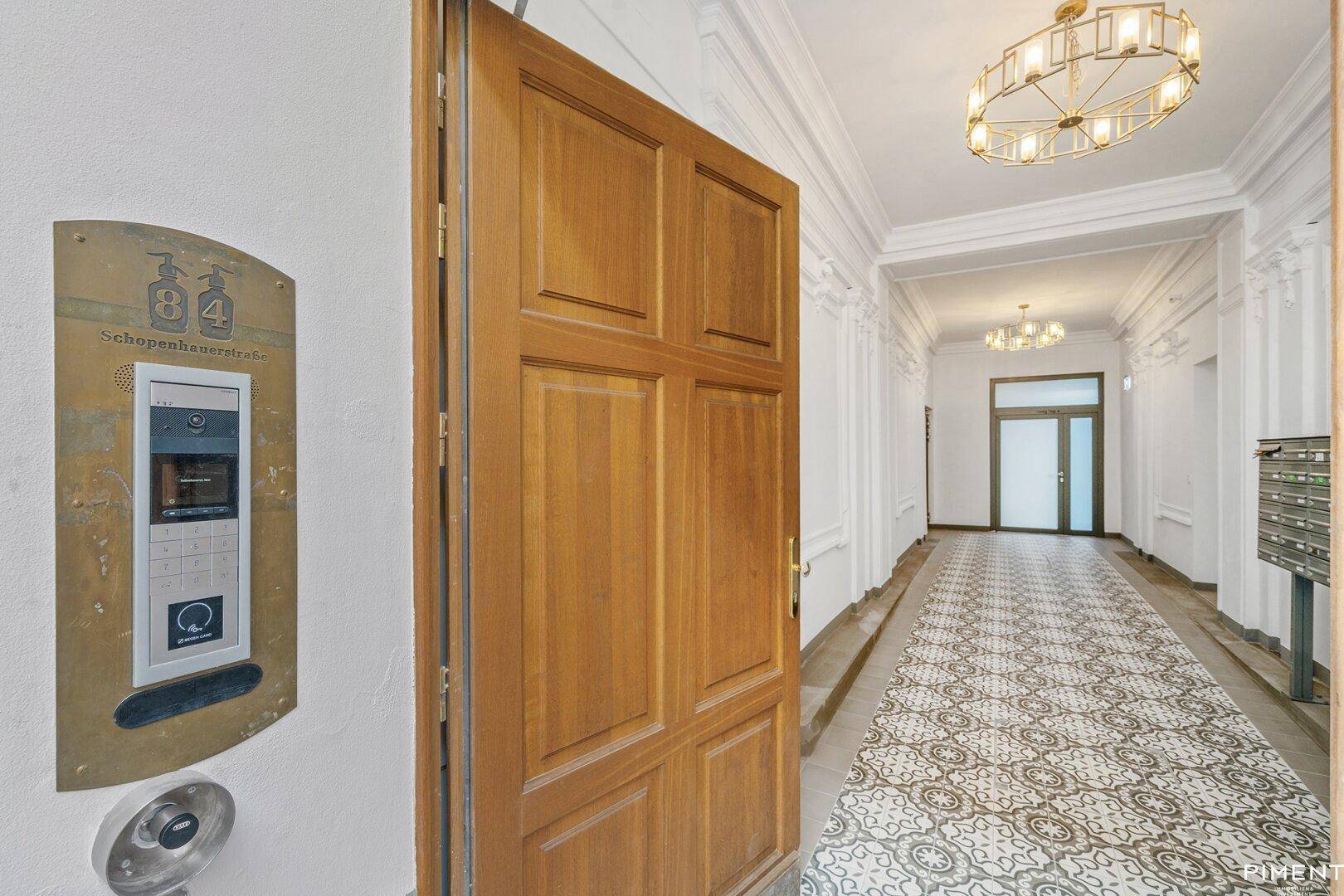 Eleganter Eingangsbereich mit gemustertem Fliesenboden, Stuckelementen und historischem Aufzug.