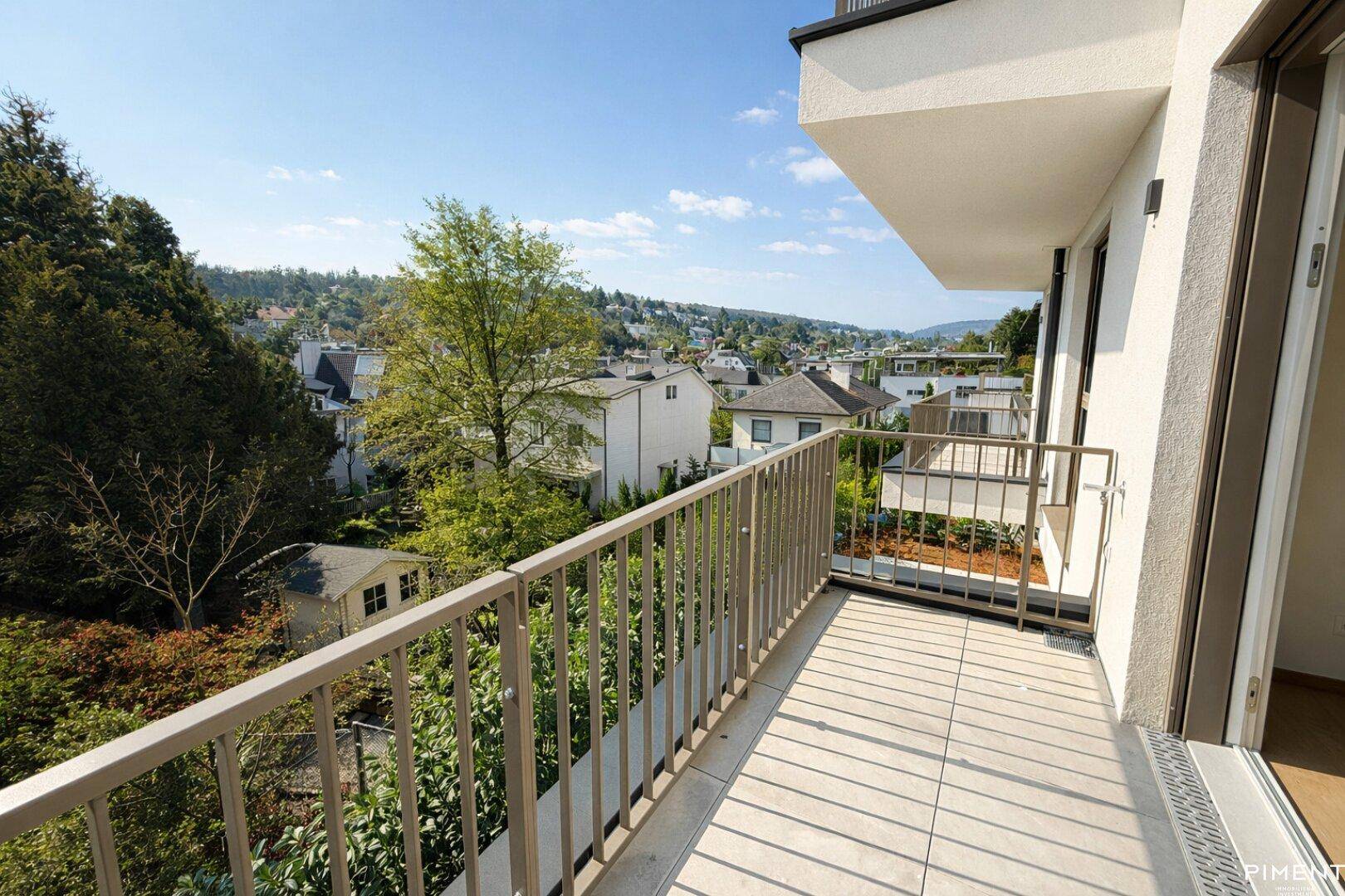 Geräumiger Balkon mit Fliesenboden und weitem Blick über die grüne Umgebung und Häuser.