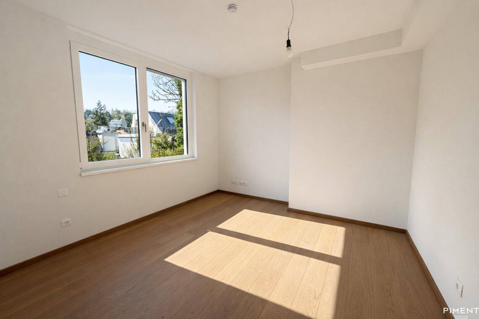 Helles Zimmer mit Parkettboden und großem Fenster, das viel Tageslicht hereinlässt.