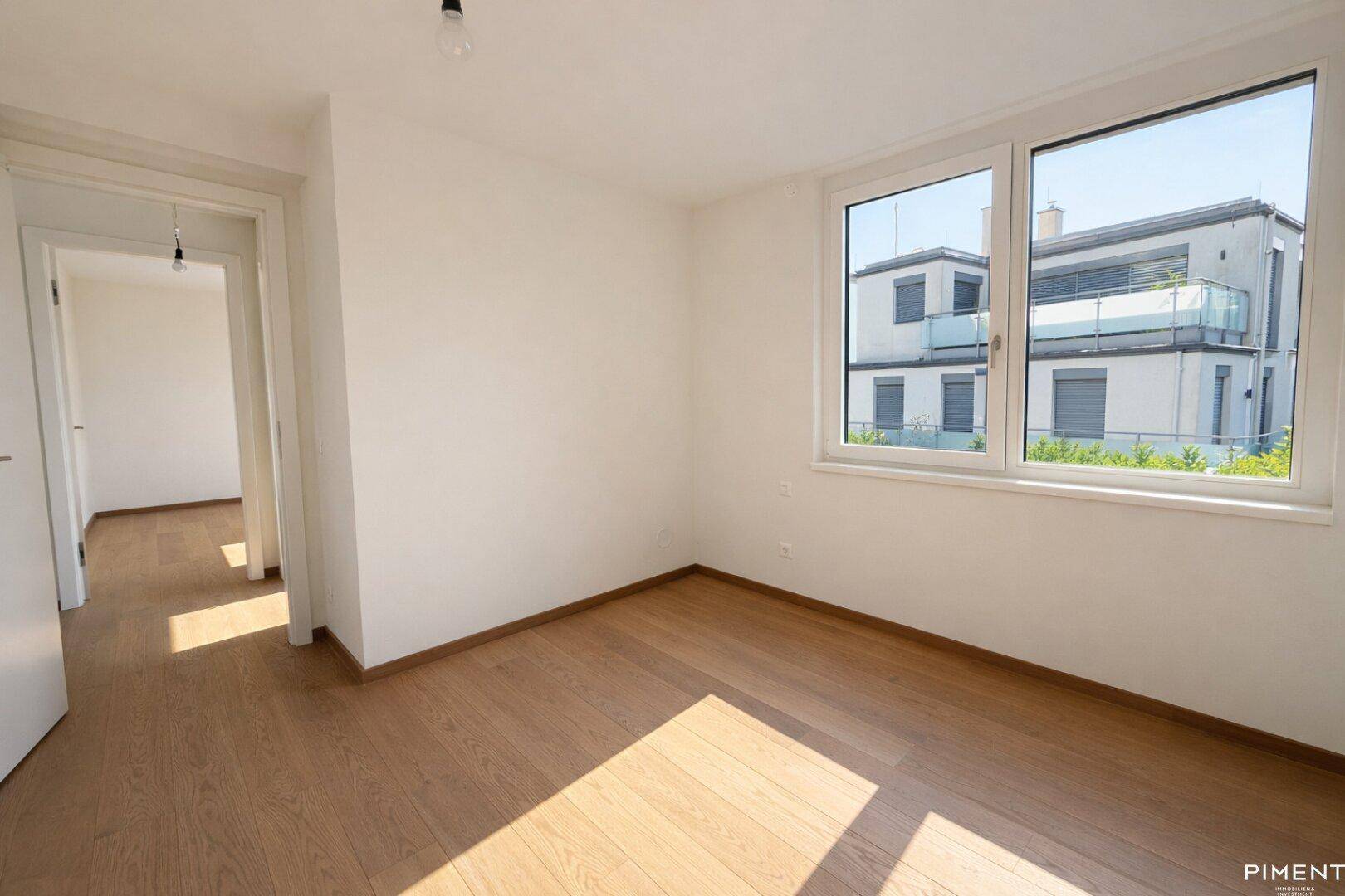 Lichtdurchflutetes Zimmer mit Holzparkett und Blick auf die moderne Wohnanlage.