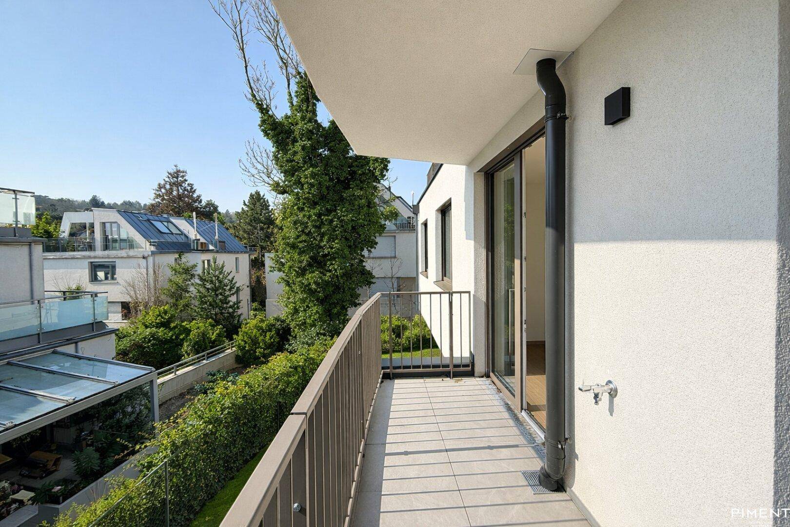 Moderner Balkon mit Fliesenboden und Blick auf die grüne Umgebung der Wohnanlage.