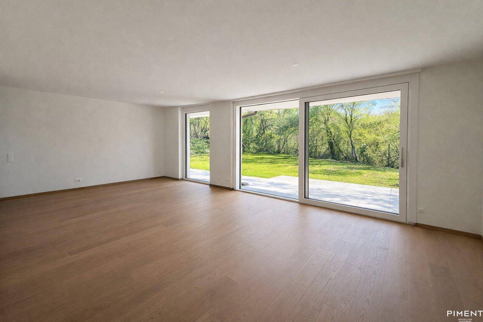 Helles, unmöbliertes Wohnzimmer mit großen Schiebetüren, Holzboden und Blick ins Grüne.