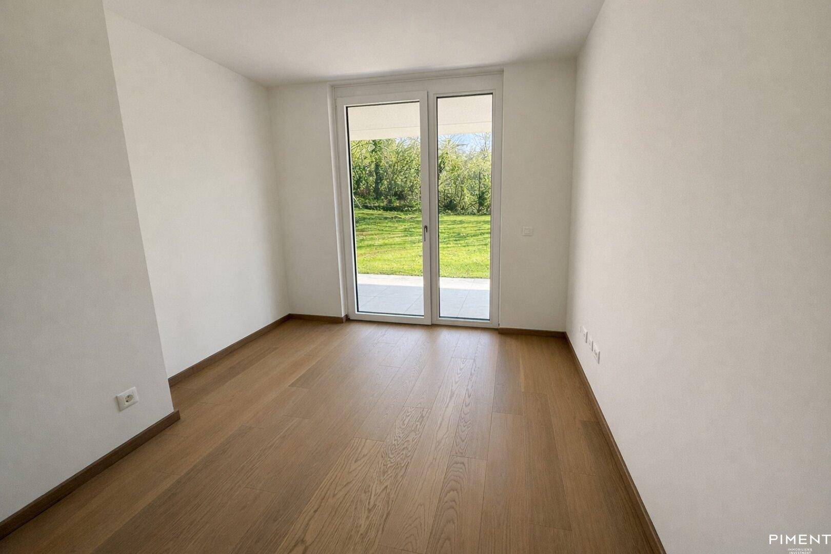 Lichtdurchflutetes Zimmer mit Parkettboden und breiter Glastür, die den Blick ins Grüne freigibt.