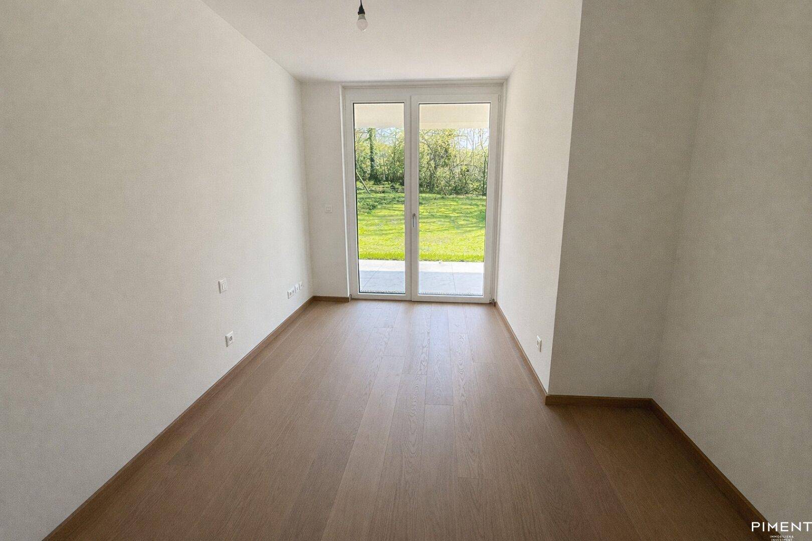 Unmöbliertes Zimmer mit Holzboden und großer Glastür, die direkten Zugang zum Außenbereich bietet.