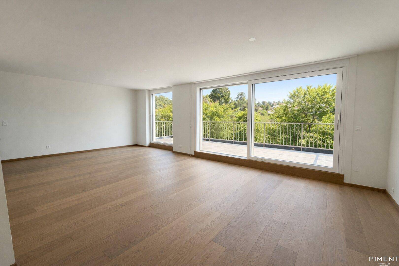 Helles, leeres Wohnzimmer mit Eichenparkett und großen Fenstern mit Zugang zur Terrasse.
