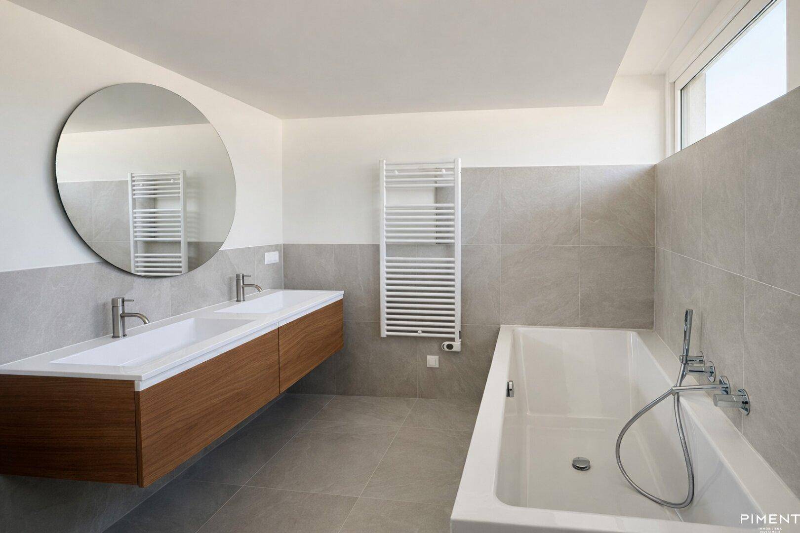Modernes Badezimmer mit Doppelwaschbecken, Badewanne und beheiztem Handtuchhalter.