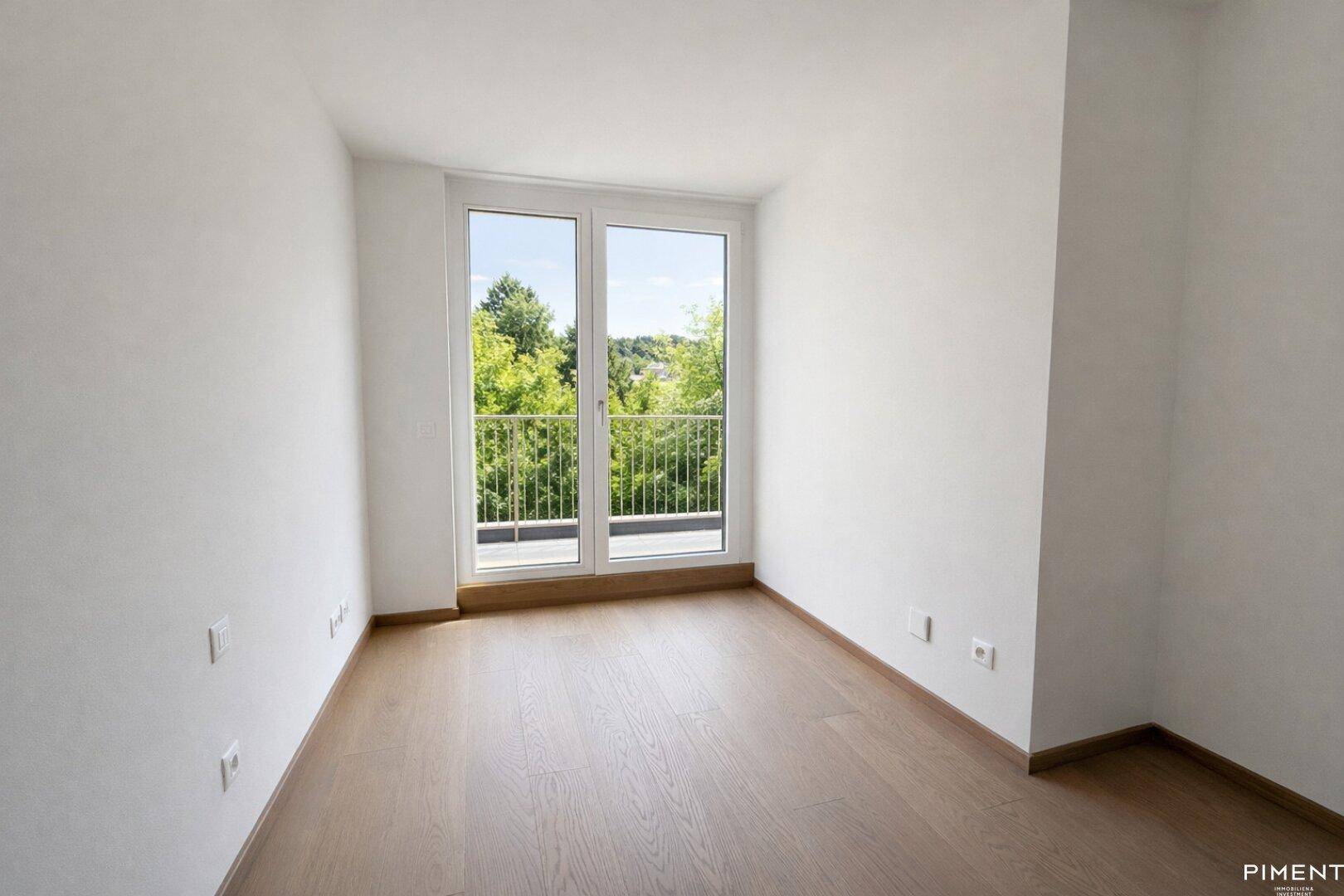 Helles Schlafzimmer mit Holzboden und Fenstern, die einen direkten Blick ins Grüne ermöglichen.