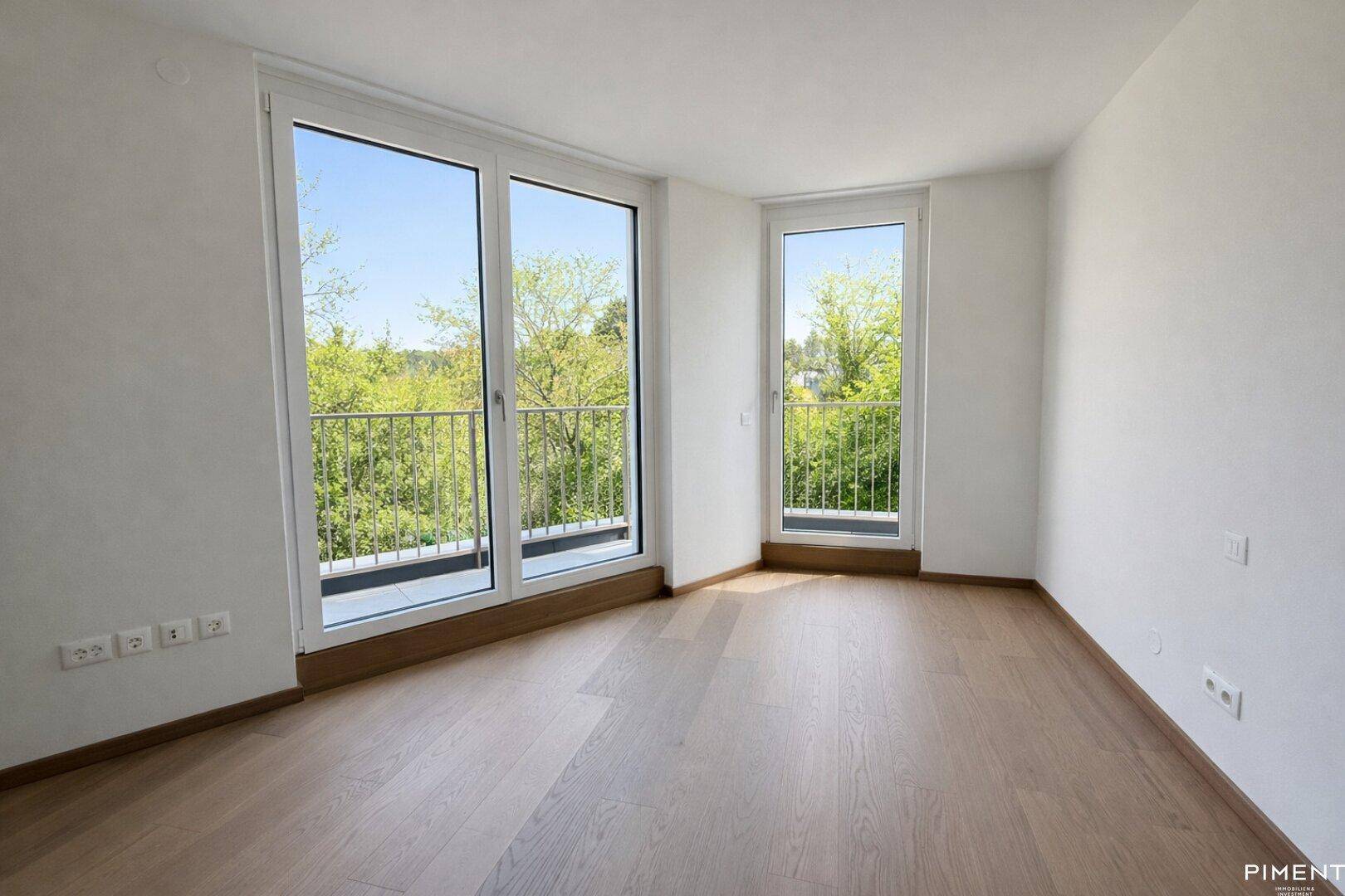 Schlafzimmer mit hellem Parkettboden und großen Fenstern, die einen grünen Ausblick bieten.
