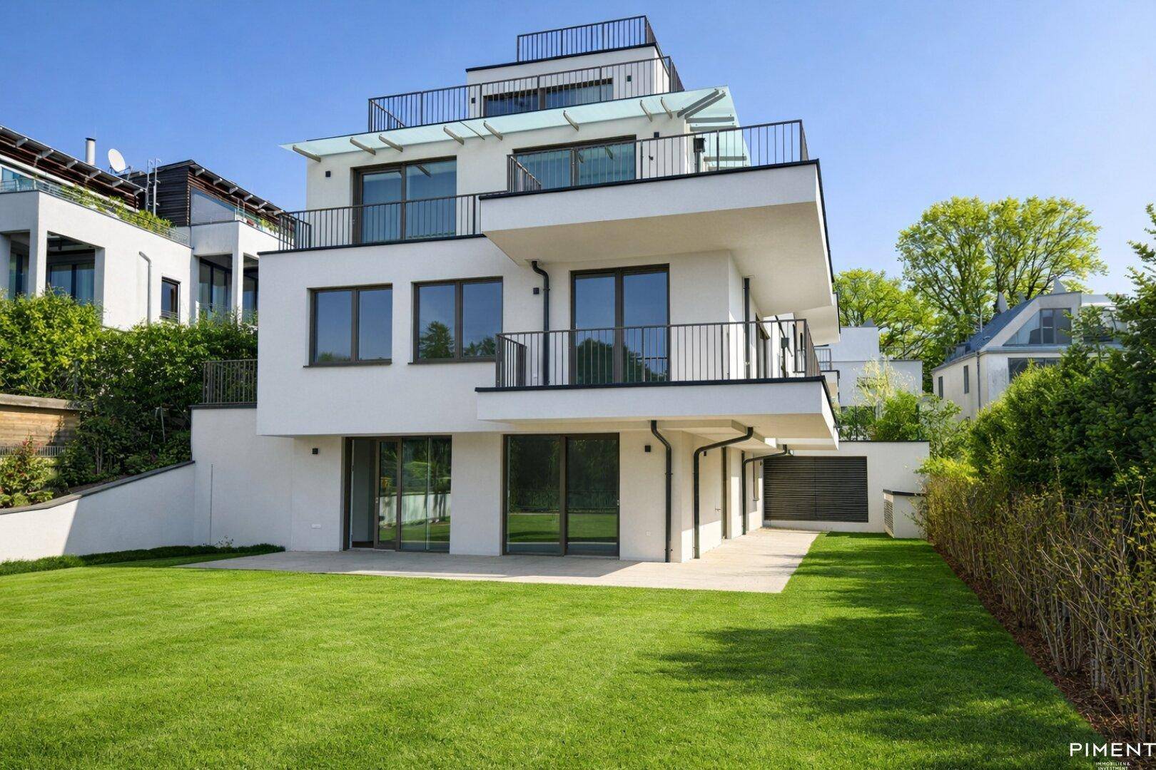 Zeitgenössisches Gebäude mit weißer Fassade, großen Fenstern und Balkonen, umgeben von einem gepflegten Garten.