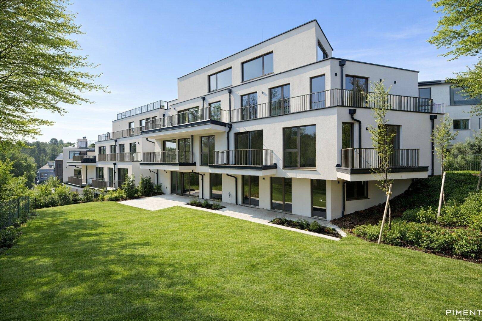 Modernes Mehrfamilienhaus mit weißer Fassade, Balkonen und großzügiger Grünfläche in sonniger Lage.