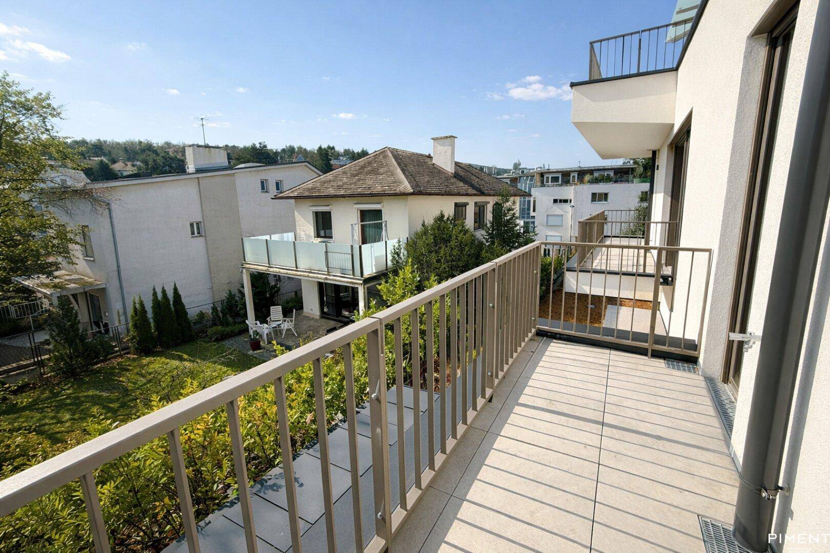 Geräumiger Balkon mit Fliesenboden und einem weiten Blick auf die grüne Umgebung und Nachbargebäude.