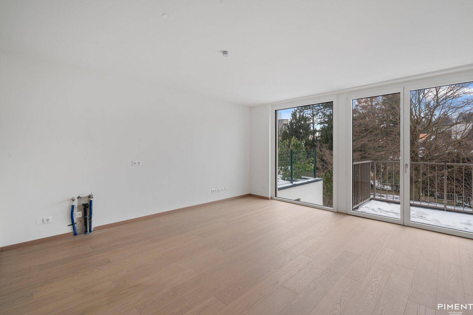 Lichtdurchfluteter Raum mit Holzboden, großen Fenstern und Balkonzugang, vorbereitet für Installationen.